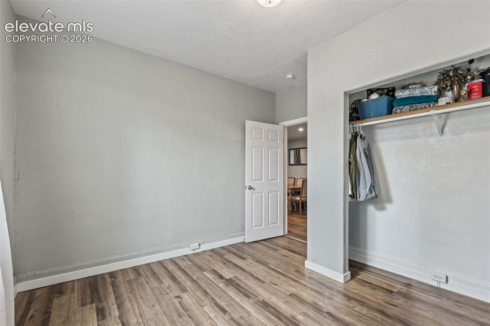 Room featuring wood-finish flooring, a neutral wall color, white baseboards, and a built-in closet with shelving and a hanging rod