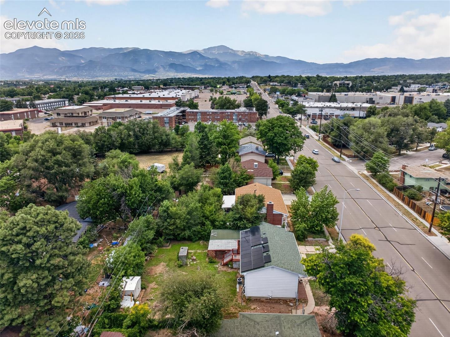 Aerial perspective featuring a residential lot with solar panels, mature trees, and mountainous scenery