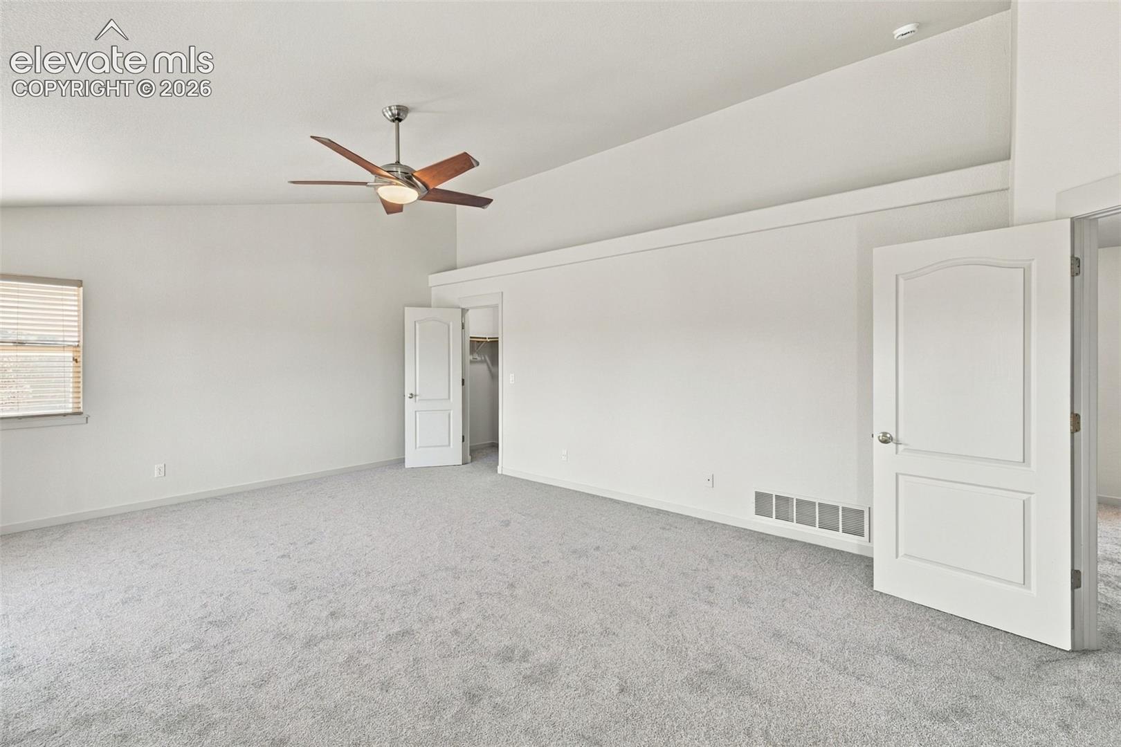 Vaulted ceilings featuring a central ceiling fan with integrated lighting, neutral wall-to-wall carpeting, and paneled interior doors