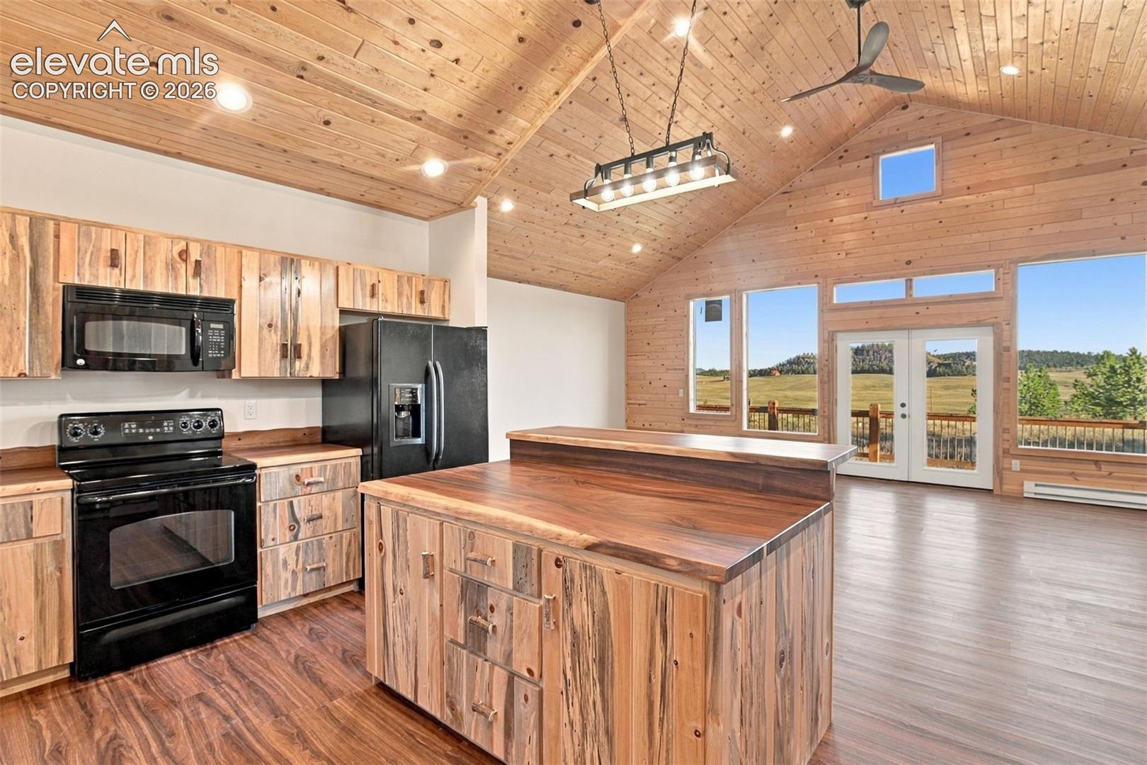 Kitchen featuring natural wood-finish cabinetry, a central island with a solid wood countertop, vaulted wood-plank ceilings, black built-in appliances, and double doors opening to a deck