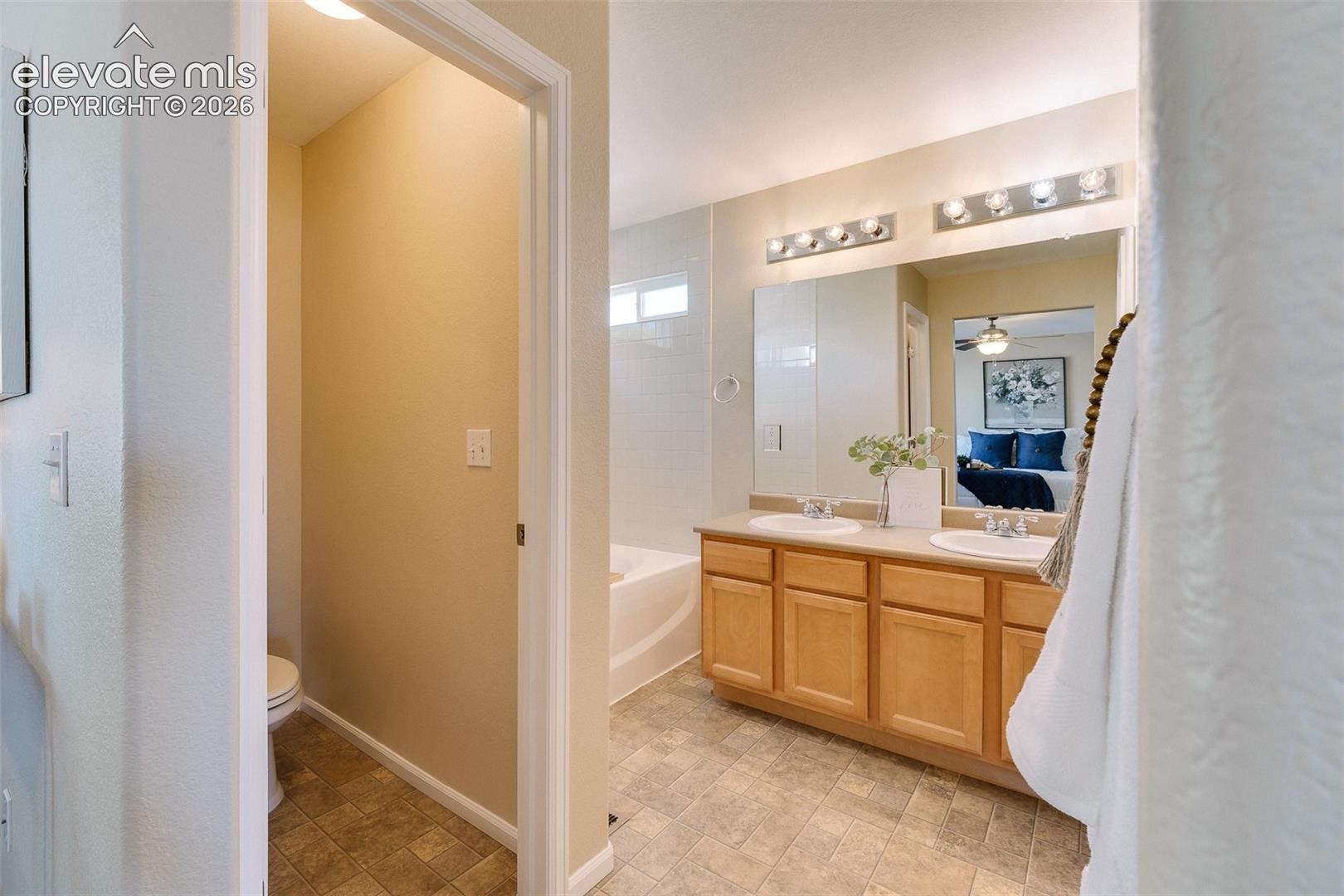 Bathroom featuring a double-sink vanity with wood-finish cabinetry, a full-width mirror, dual light fixtures, and a combined tub and shower surround