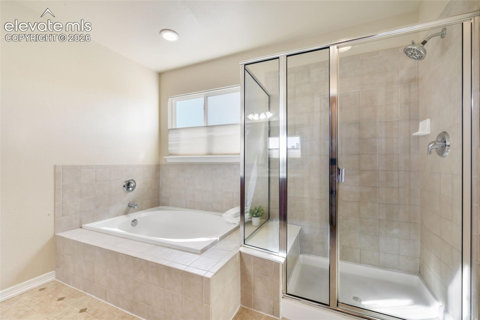 Built-in soaking tub with tile surround, separate glass-enclosed shower with tile walls, and recessed lighting