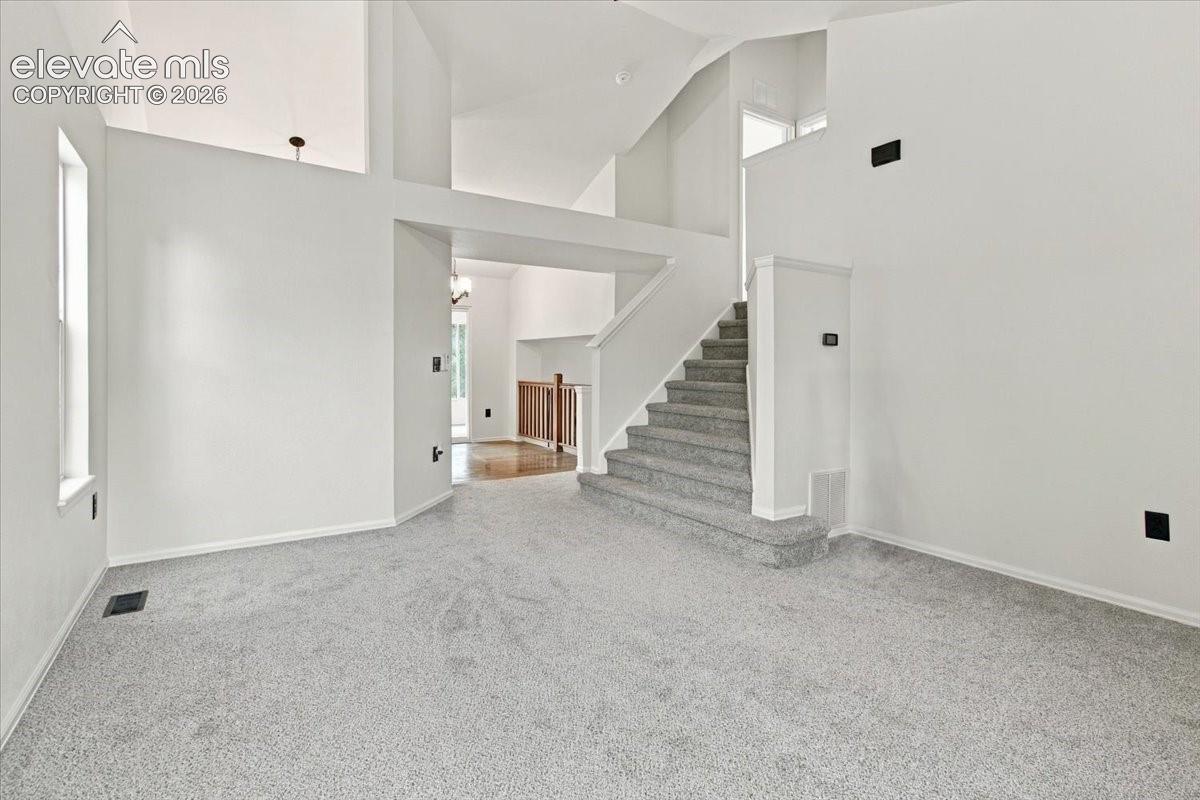 Vaulted ceilings, carpeted staircase, neutral wall palette, vertical windows, and wood-finish flooring