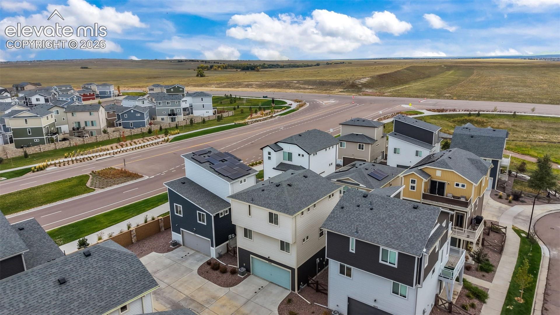 Aerial perspective featuring multi-story residential architecture with shingle roofing, attached garages, concrete driveways, and installed rooftop solar panels
