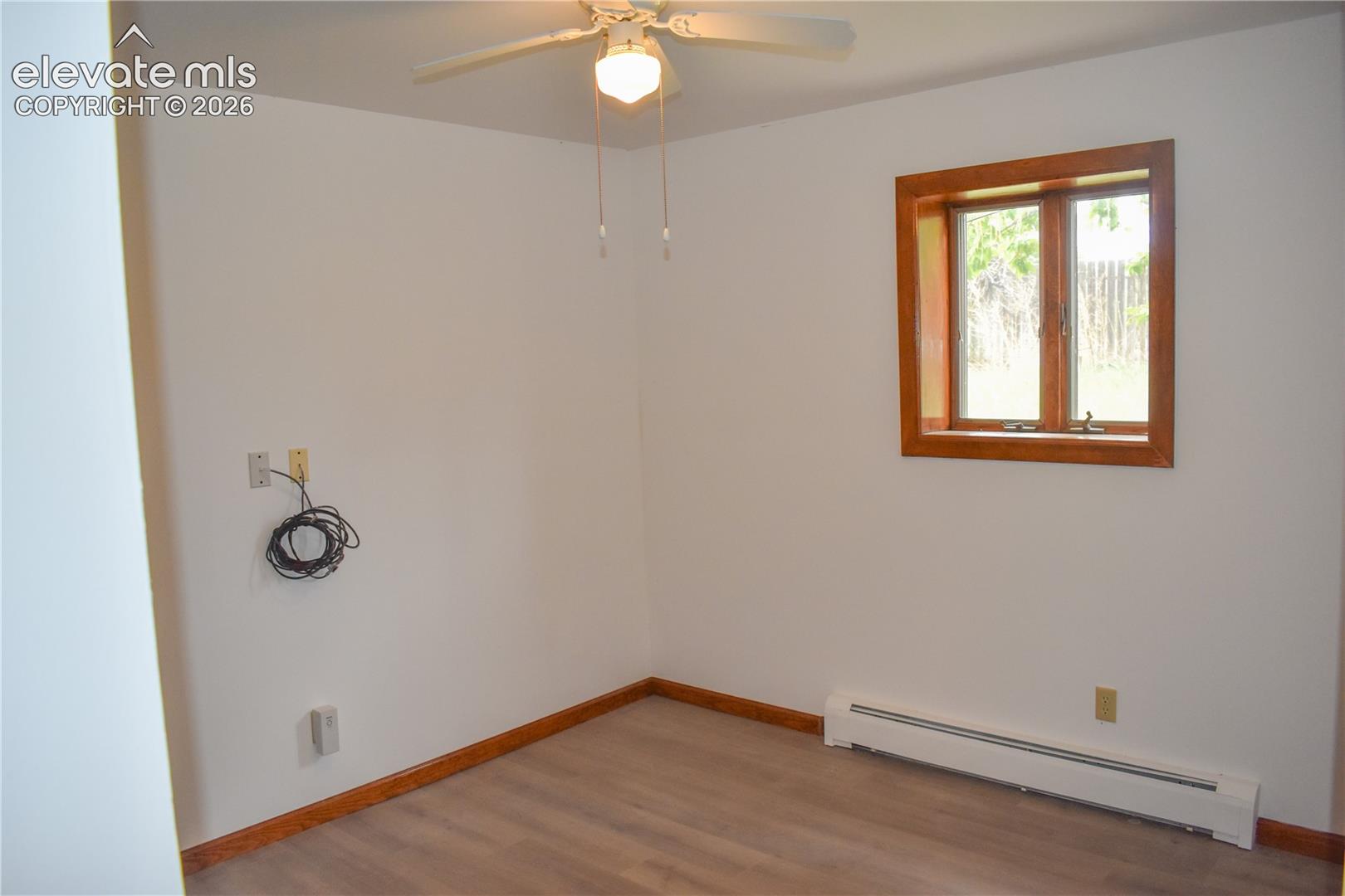 Neutral wall paint with wood-finish flooring, a window featuring wood trim, and a ceiling fan with integrated lighting
