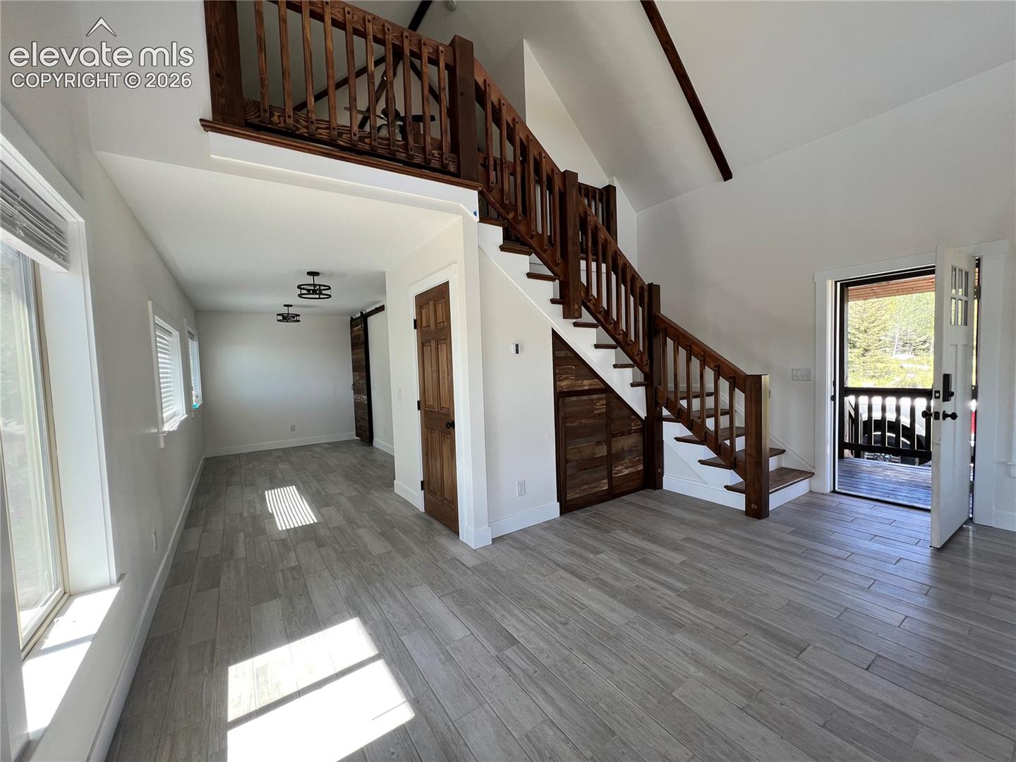 Vaulted ceilings, wood-finish flooring, wood staircase with a matching loft railing, and a wood barn door
