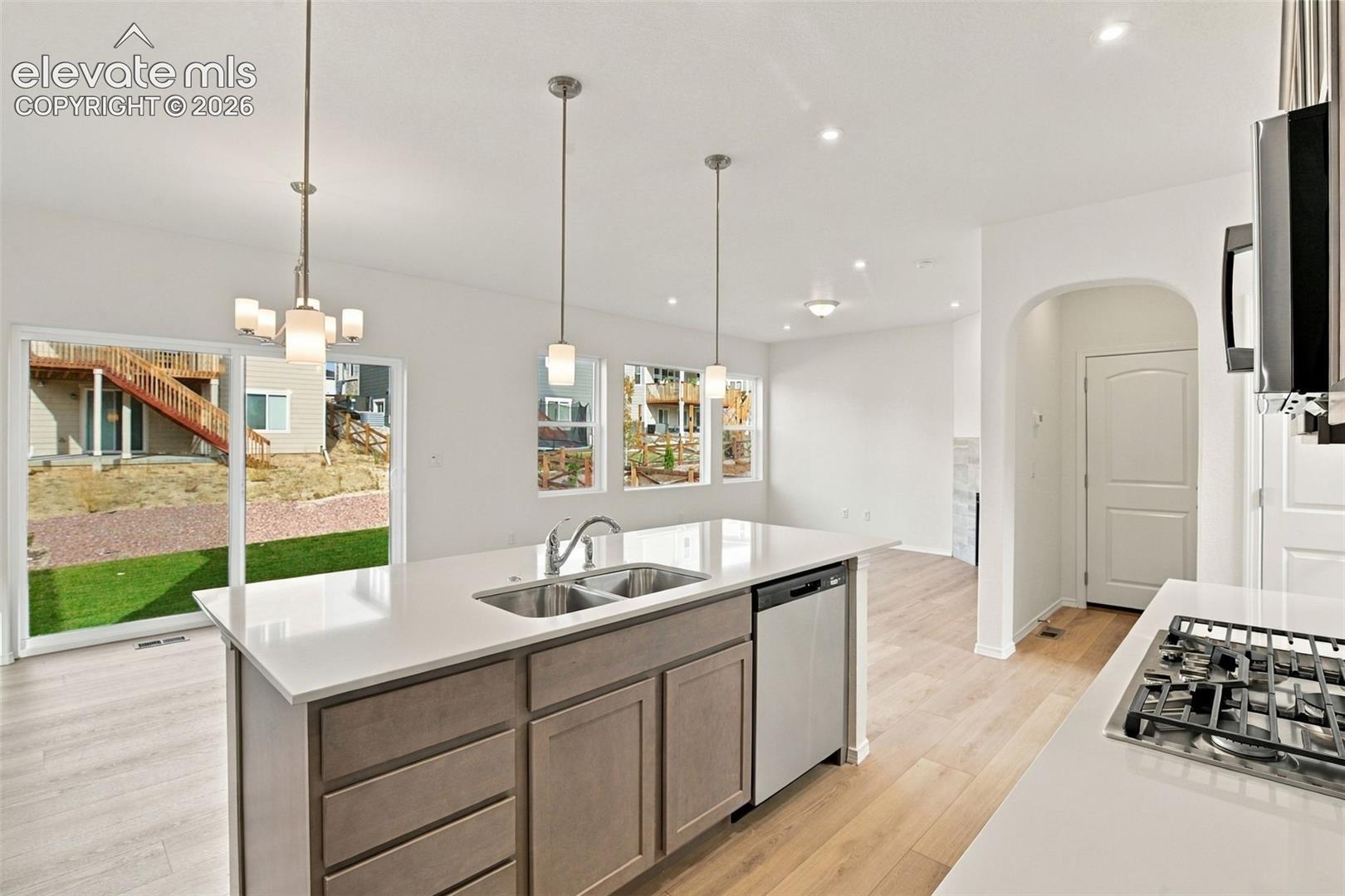 Kitchen featuring an island with stone-finish countertops, stainless steel dual-basin undermount sink, pendant lighting, built-in dishwasher, and wood-finish flooring