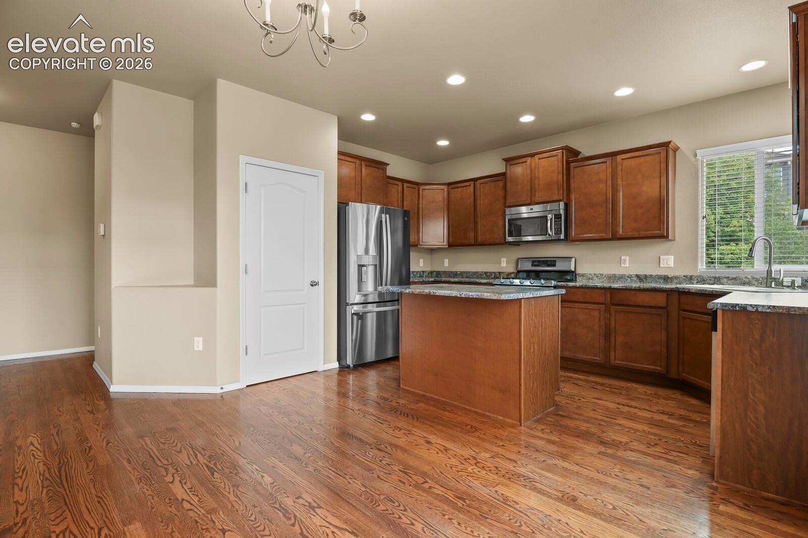 Kitchen featuring wood-finish flooring, recessed lighting, wood cabinetry, stone countertops, and stainless steel appliances
