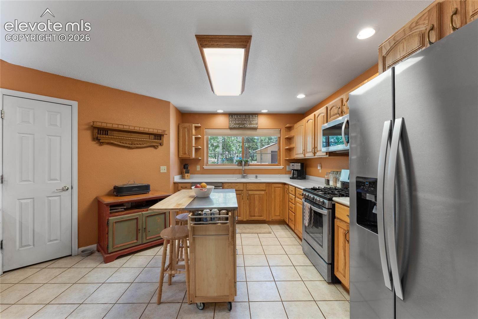 Kitchen featuring tile flooring, wood cabinetry, stainless steel appliances, and a window with outdoor scenery