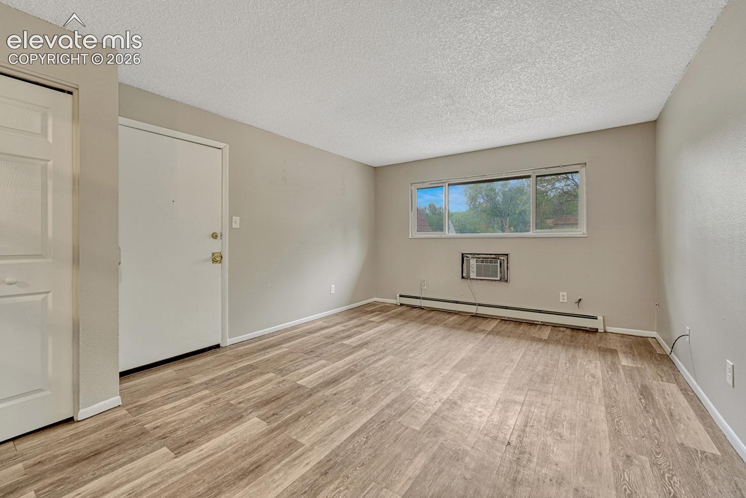 Wood-finish flooring, neutral wall paint, window with exterior exposure, and a wall-mounted air conditioning unit