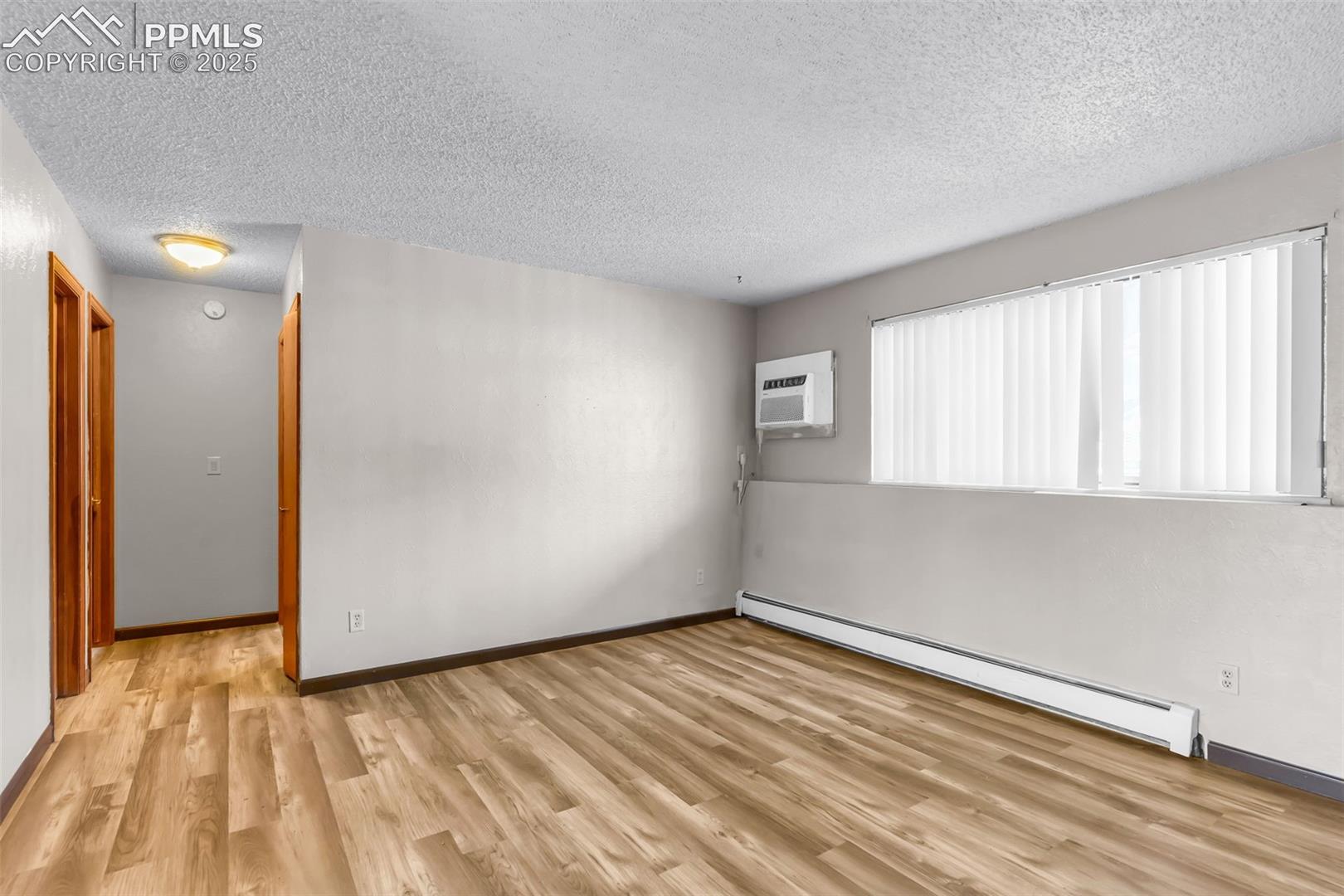Unfurnished room with a textured ceiling, baseboard heating, light wood finished floors, and an AC wall unit