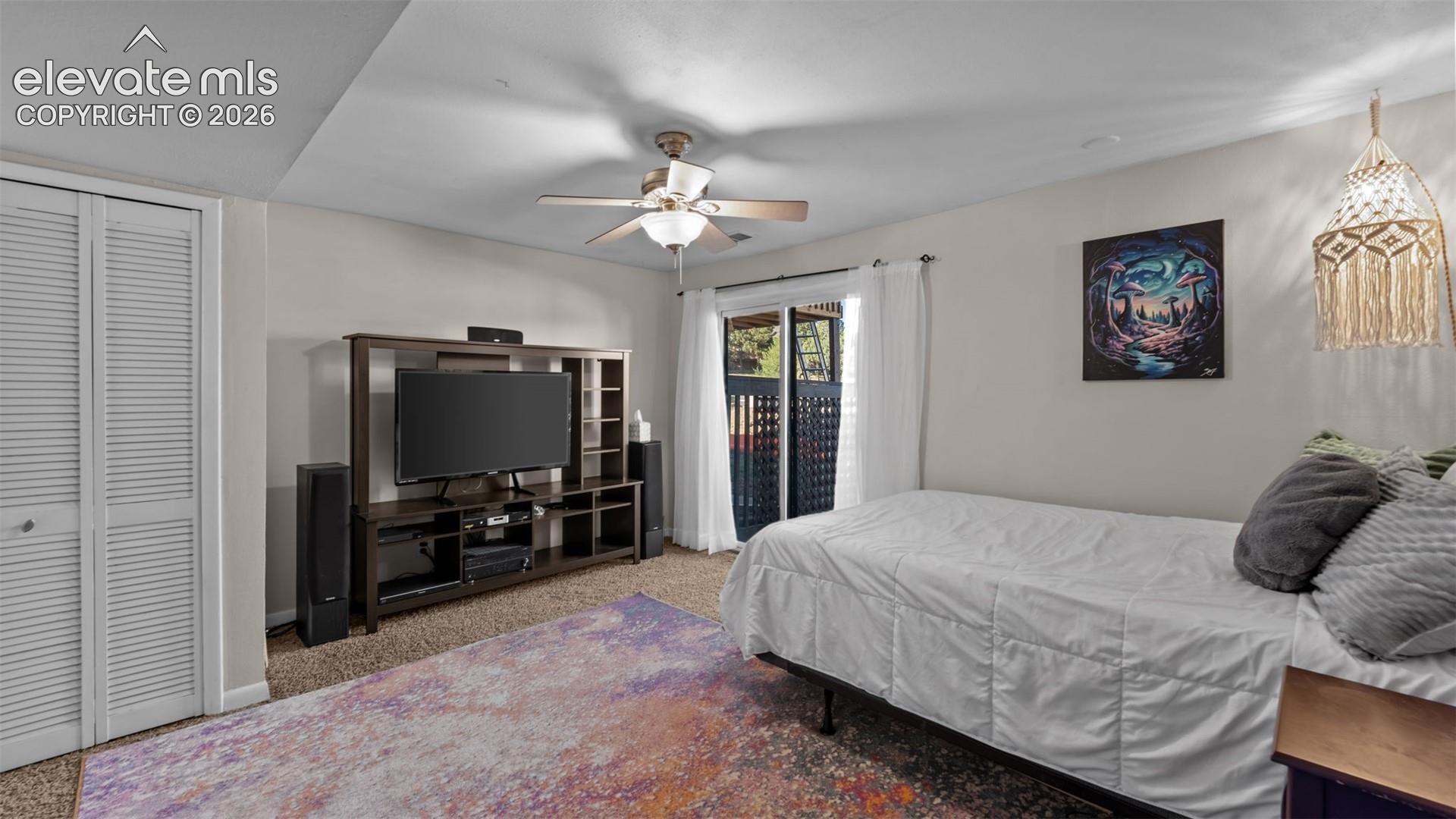 Interior space featuring carpeting, ceiling fan with integrated lighting, and white louvered-panel closet doors, with sliding glass doors providing access to the exterior