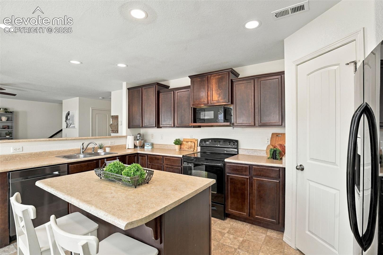 Kitchen featuring dark wood cabinetry, light-toned countertops, a stainless steel sink, and recessed lighting