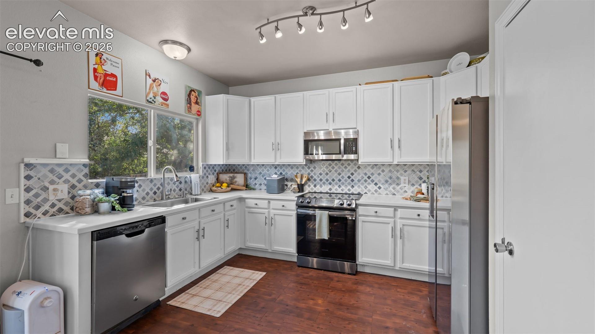 Kitchen with white cabinetry, stainless steel appliances, a patterned tile backsplash, and wood-finish flooring