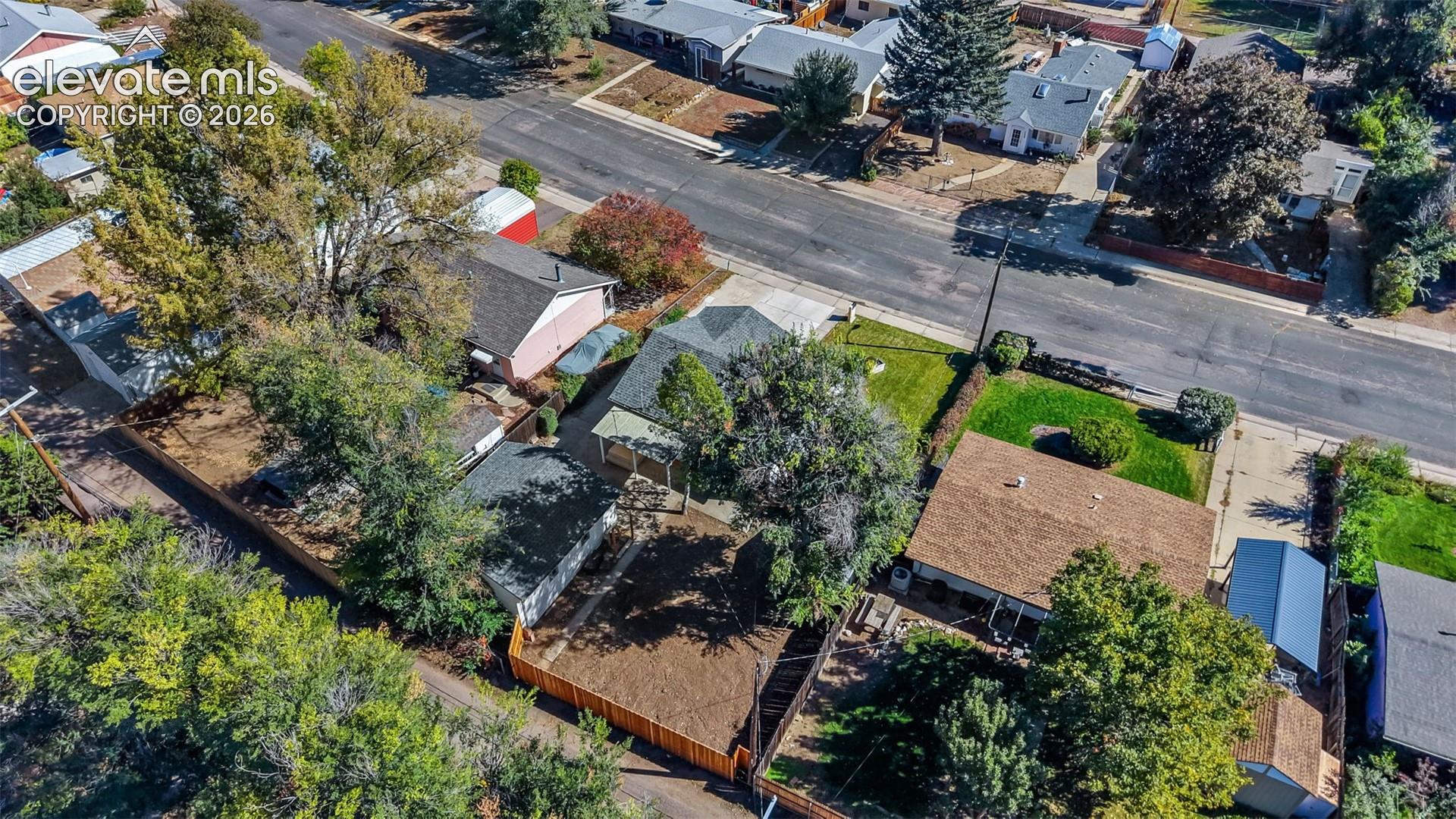Aerial perspective of a property featuring a composition shingle roof, a concrete driveway, a wood-fenced rear yard, mature trees, and a detached outbuilding