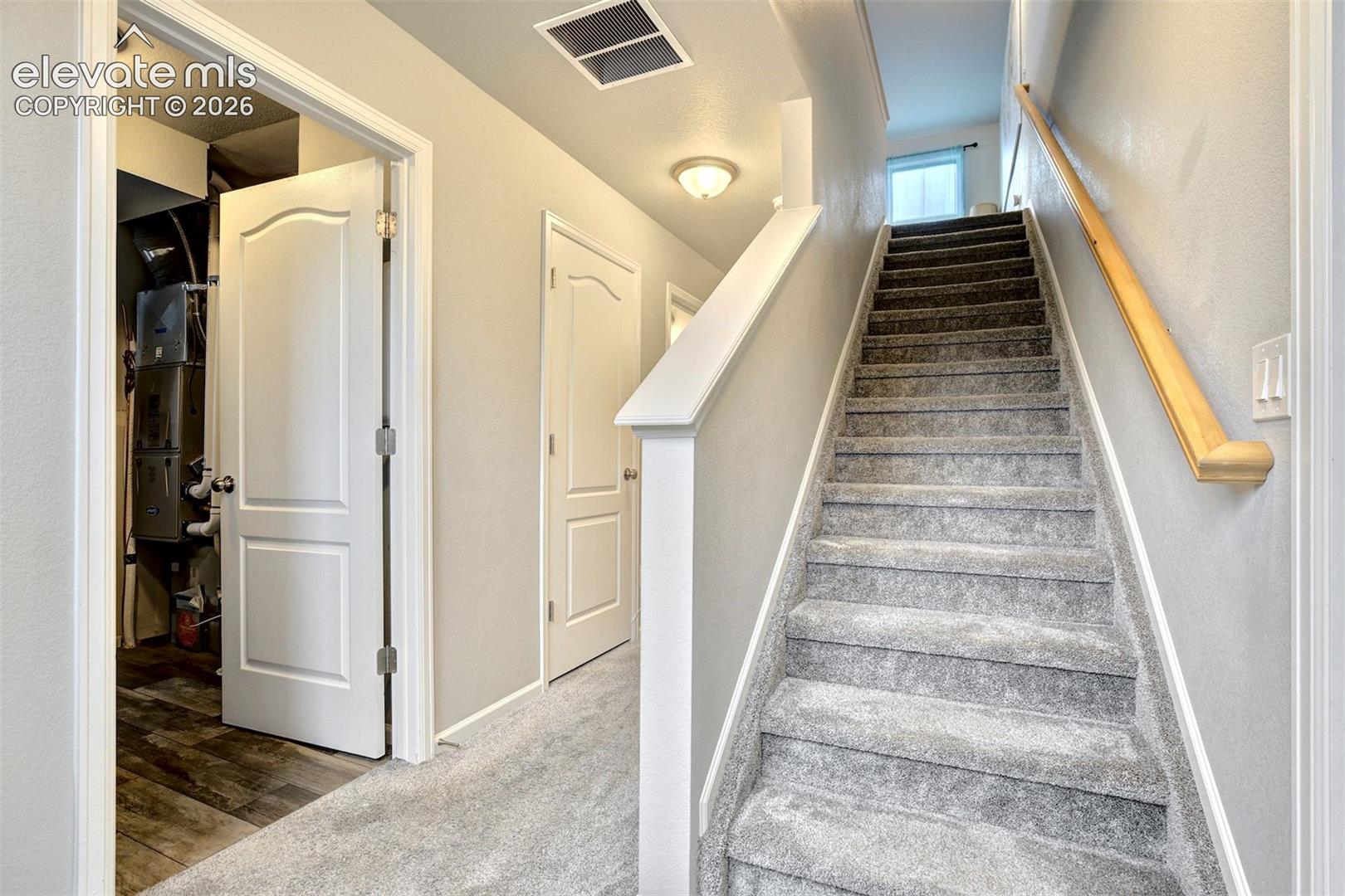 Staircase featuring wall-to-wall carpeting and a natural wood handrail, accented by interior doors with arched-panel detailing and flush-mount lighting