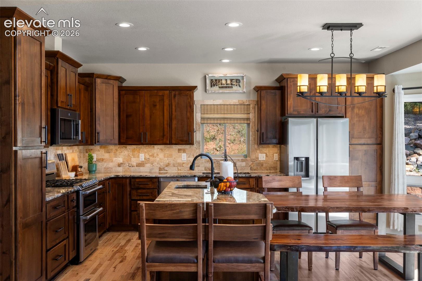 Kitchen featuring light stone counters, stainless steel appliances, light wood-style flooring, pendant lighting, and recessed lighting