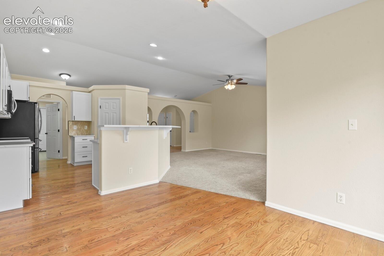 Kitchen and lEat in Dining area featuring wood-finish flooring, a breakfast bar, white cabinetry, recessed lighting, and vaulted ceilings