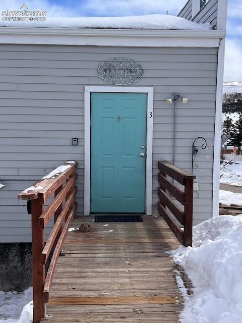 Exterior entryway featuring light gray horizontal siding, a solid wood-plank walkway, and dual-rail wood fencing