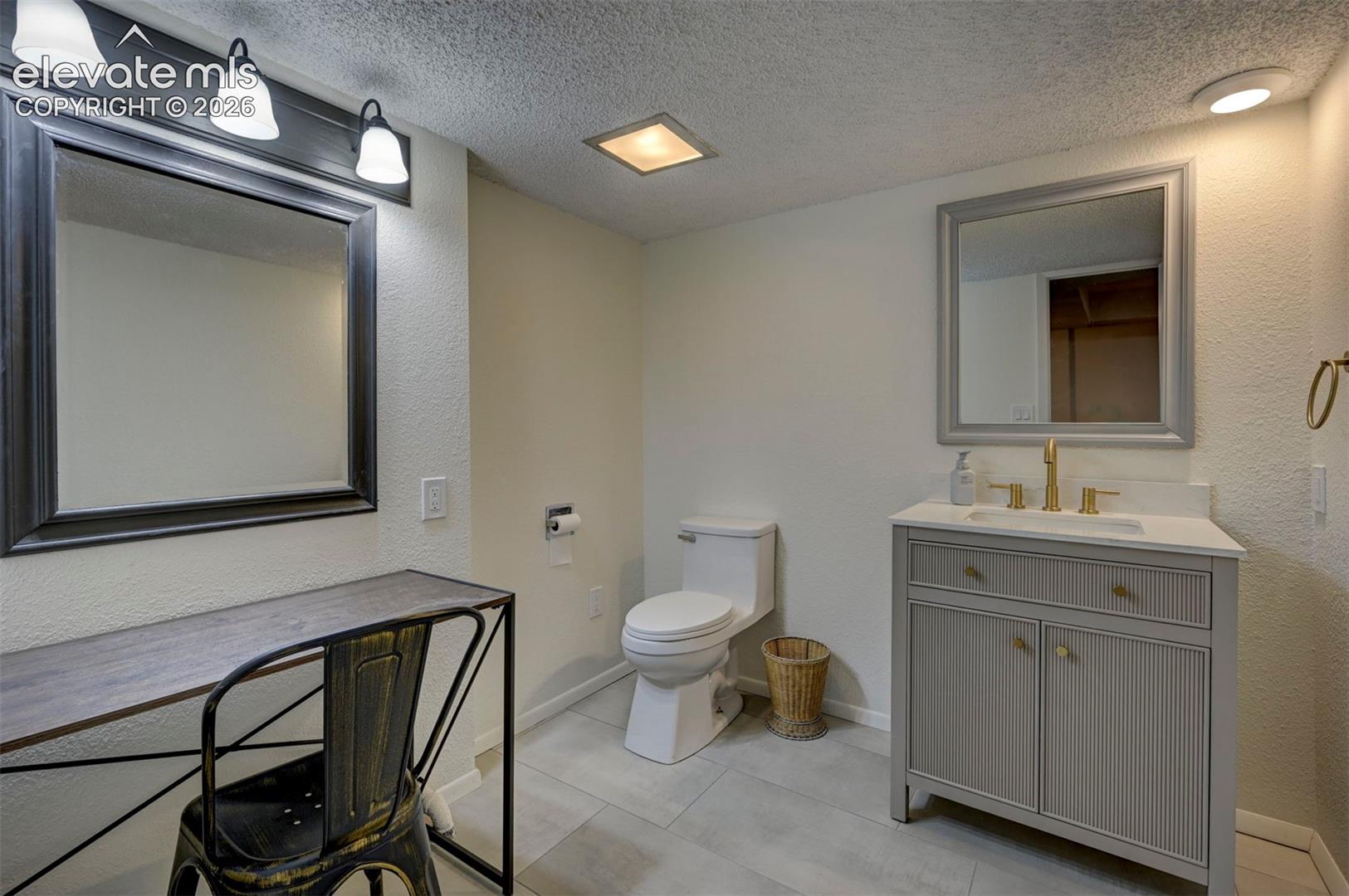 Bathroom featuring a vanity with a light-colored countertop and integrated sink, gold-toned faucet, large rectangular mirror with a grey frame, and large-format tile flooring