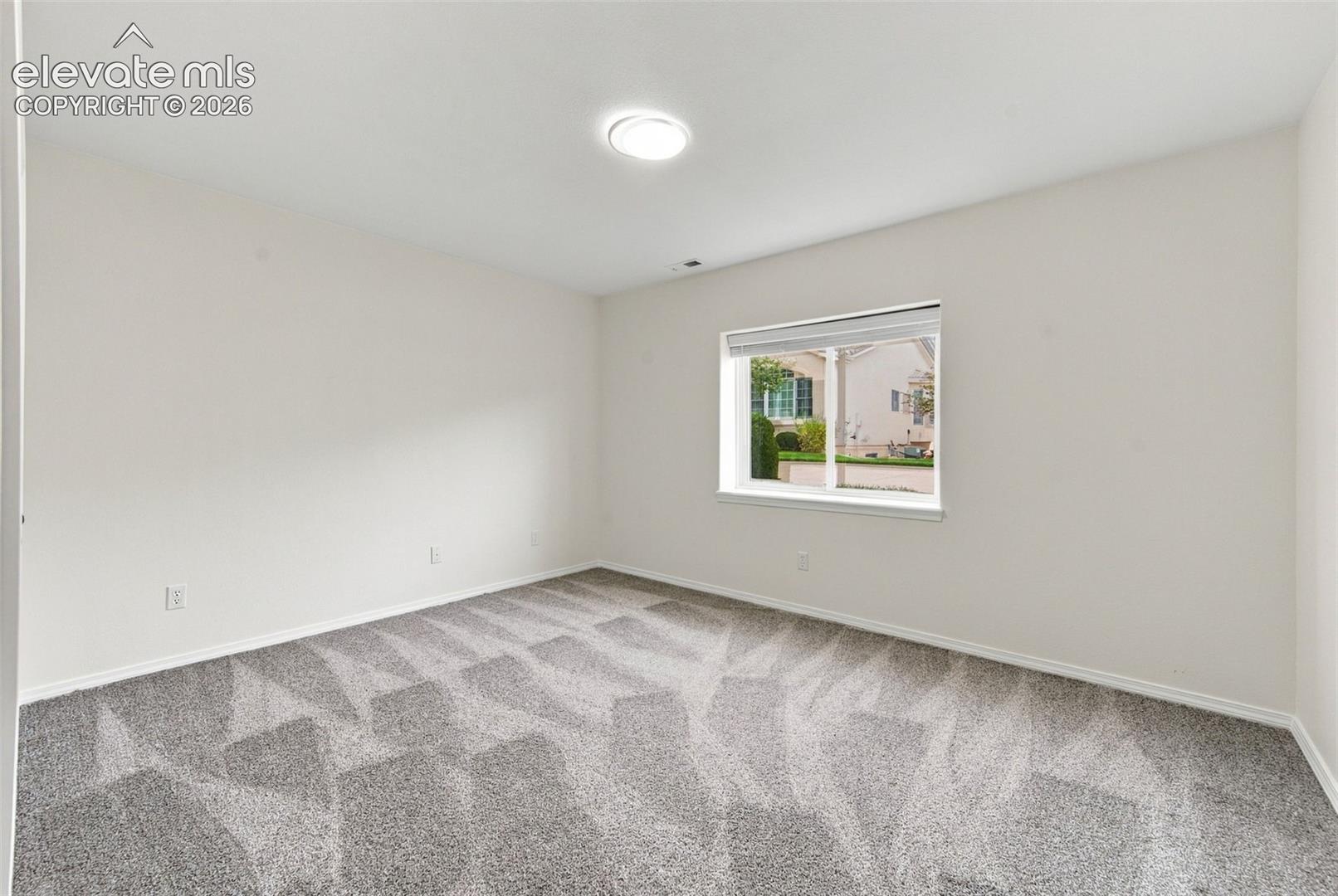Neutral-toned interior space featuring wall-to-wall carpeting, a flush-mount ceiling light fixture, and a window with white trim