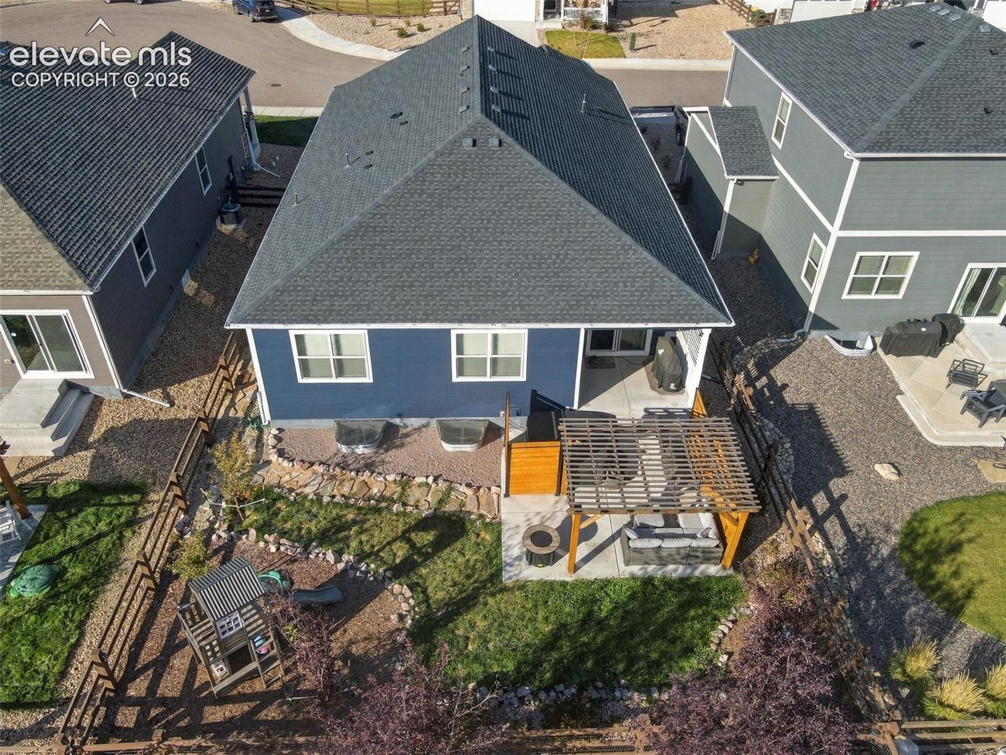 Rear exterior featuring a concrete patio with a wooden pergola, fenced yard, and stone-accented landscaping