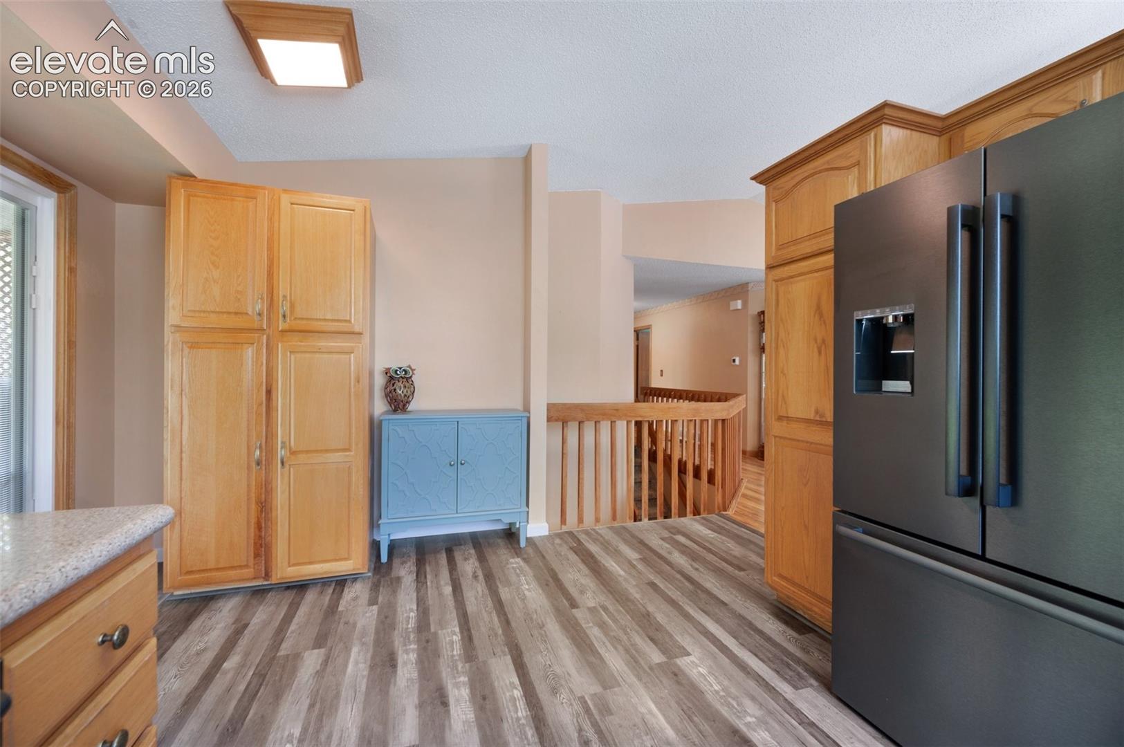 Kitchen featuring stainless steel refrigerator with ice dispenser, light wood finished floors, light stone counters, and light brown cabinetry
