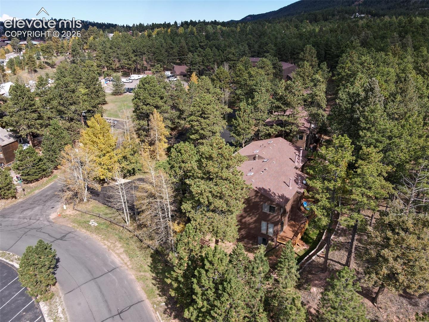 Property surrounded by mature evergreen and deciduous trees, with a visible multi-level structure featuring a brown roof and exterior