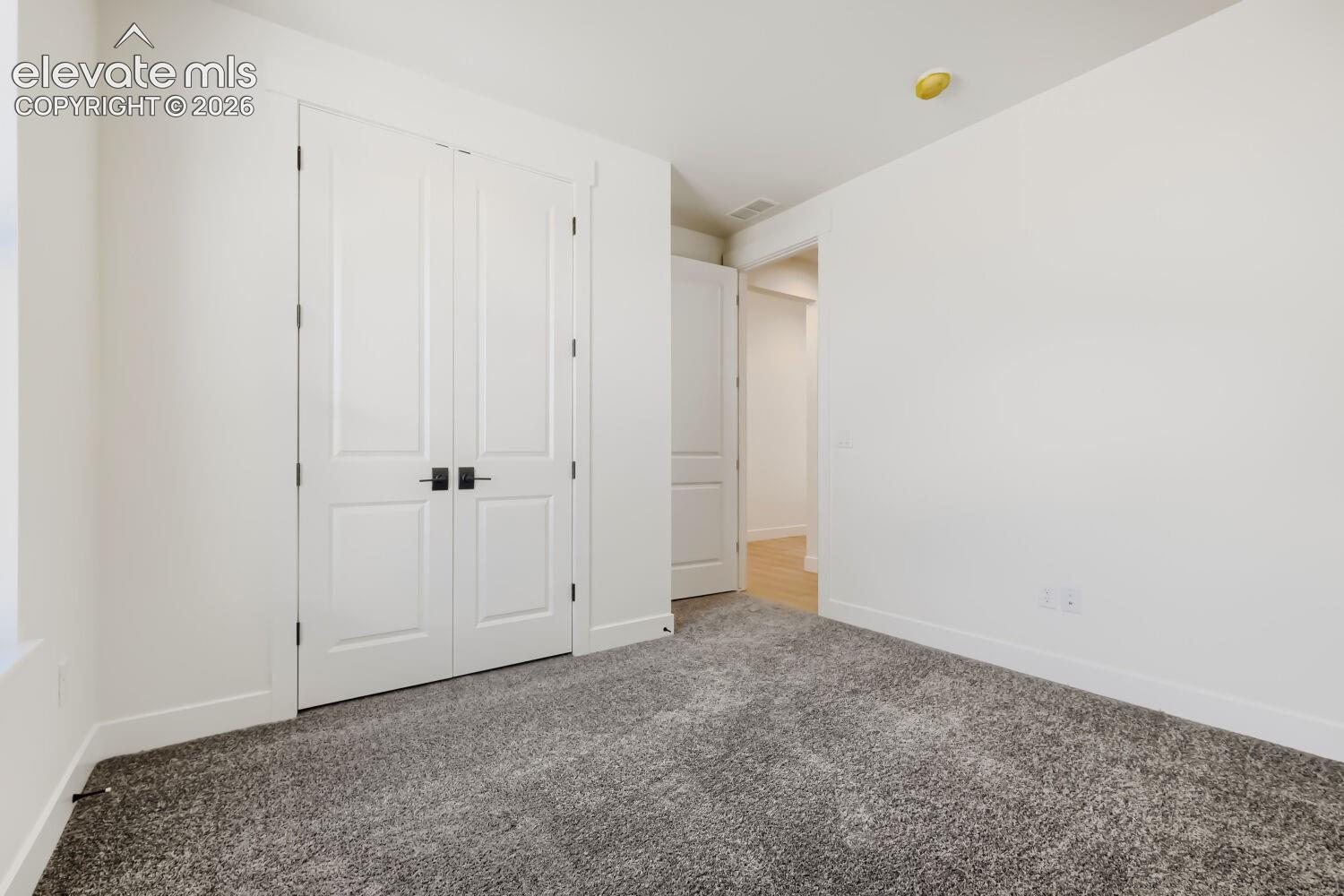 Neutral wall paint, gray carpet flooring, white trim, and white paneled doors with black hardware