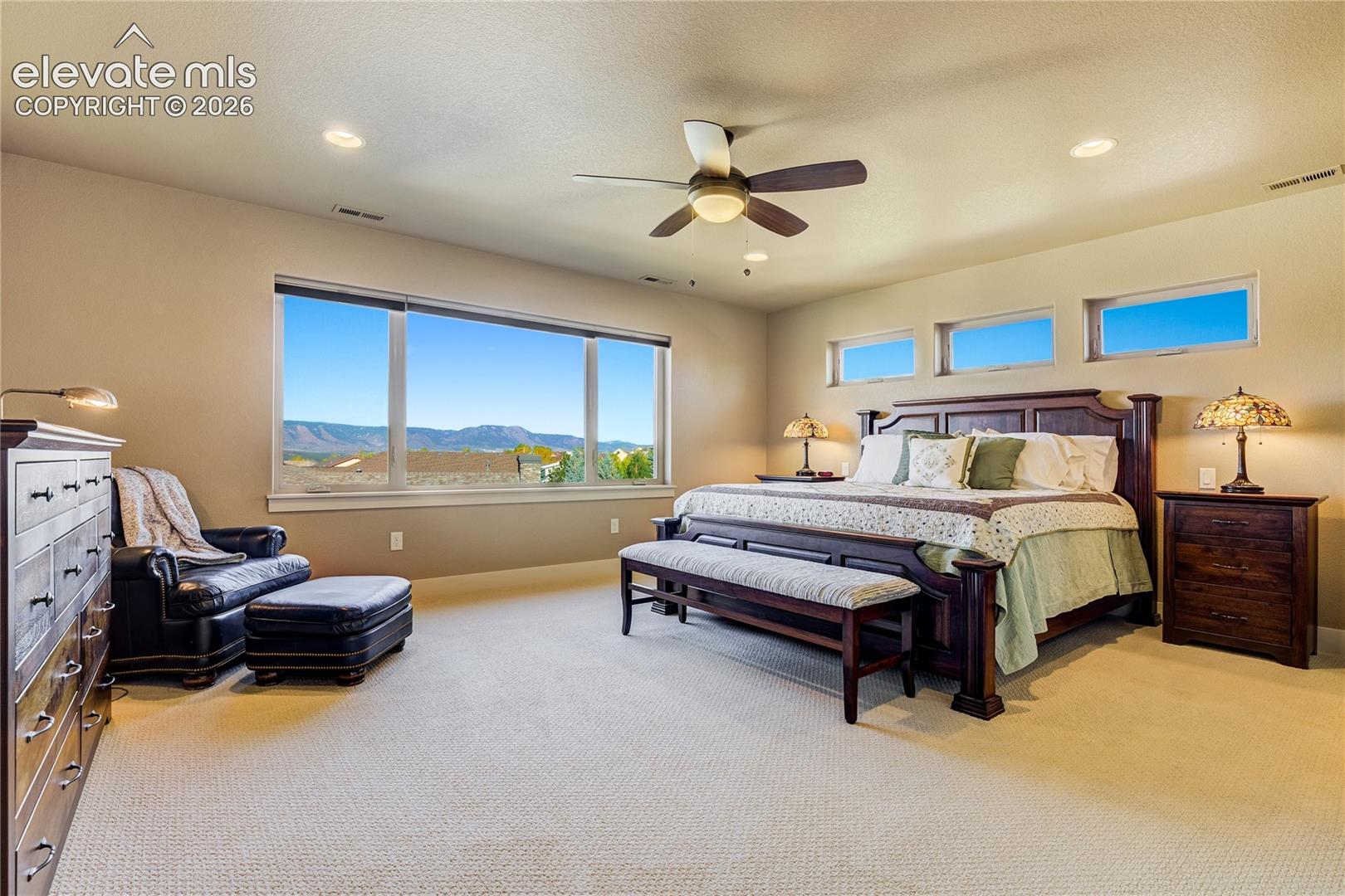 The spacious primary bedroom offers a peaceful retreat with a comfortable sitting area + breathtaking Pikes Peak, Front Range and Air Force Academy views.
