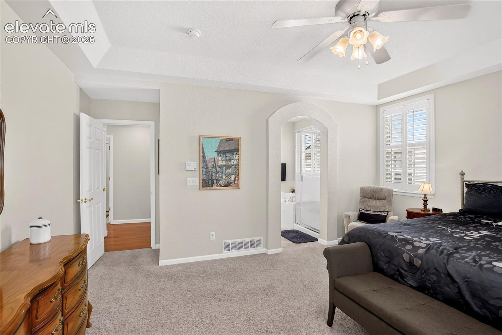 Tray ceiling with a ceiling fan light fixture, arched doorway, and plantation shutters
