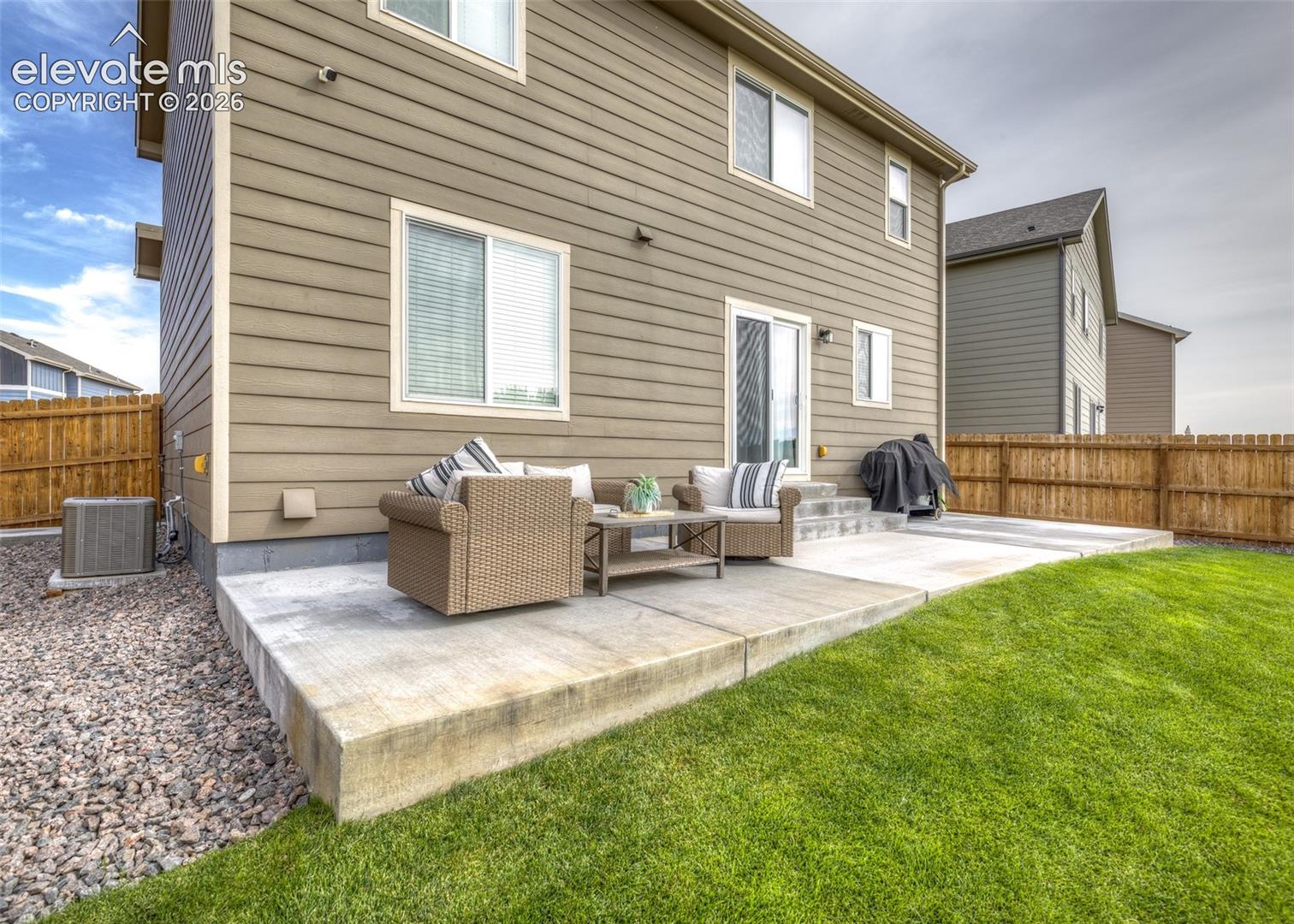 Rear elevation featuring horizontal lap siding, concrete patio, grass lawn, and wood-panel privacy fencing