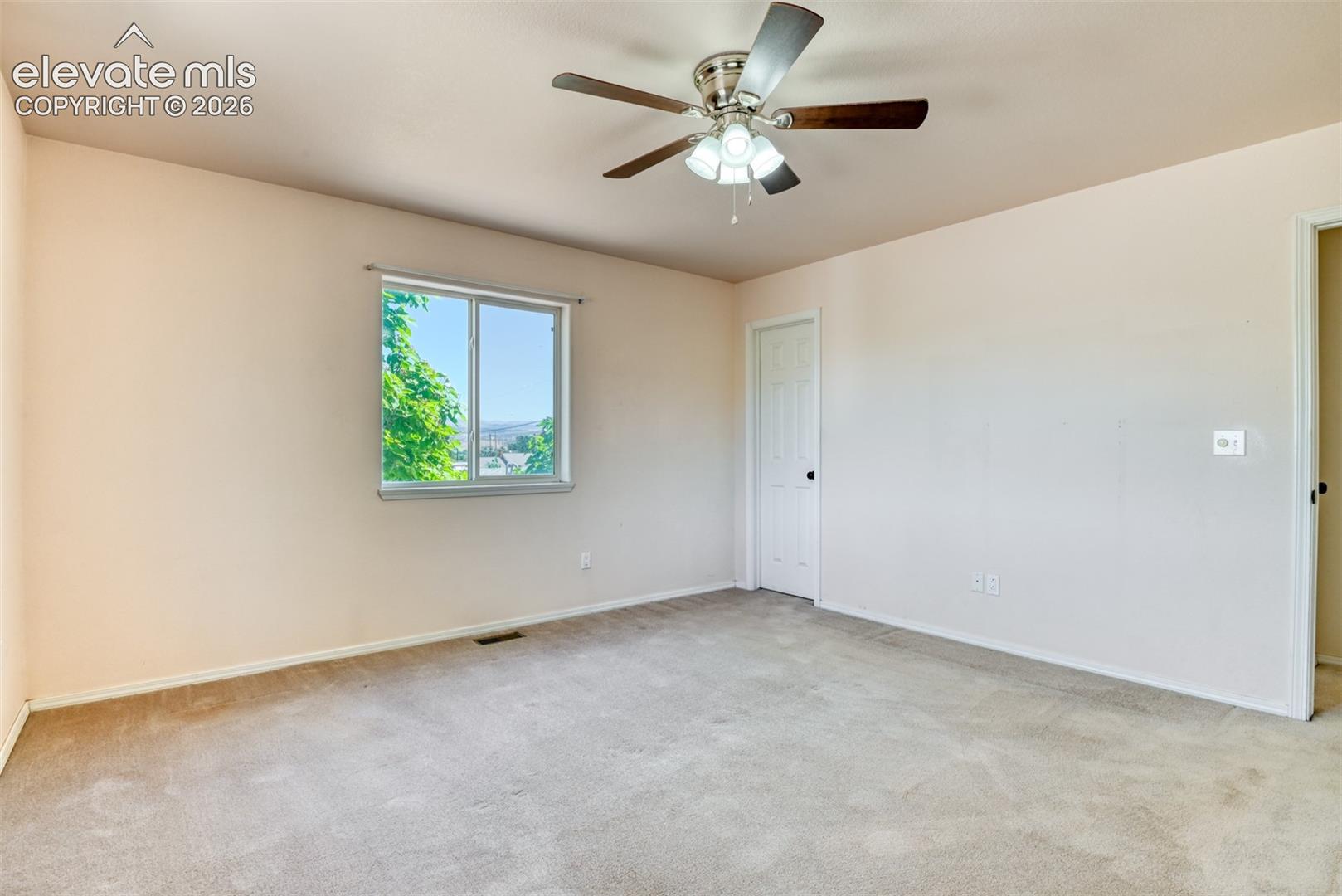 Neutral-toned room featuring neutral wall-to-wall carpeting, a multi-blade ceiling fan with integrated light fixture, a sliding window, and two interior doors