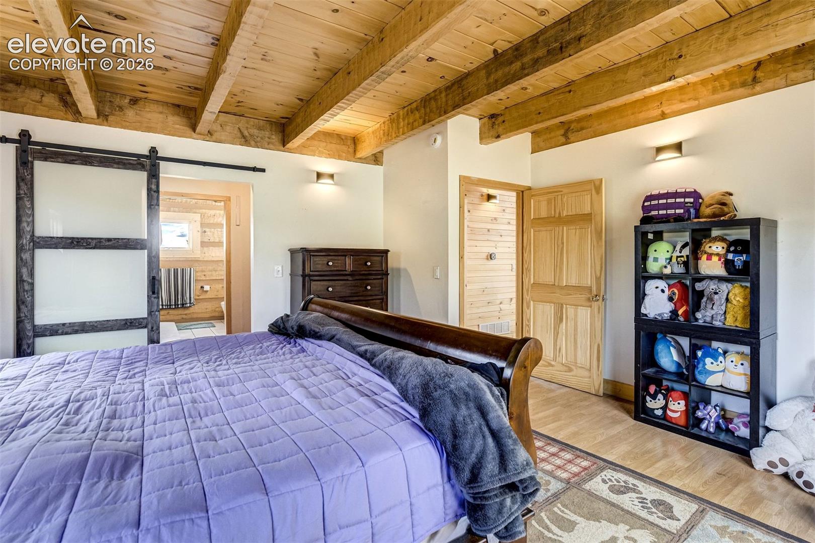 Wood-beamed ceiling with exposed trusses, wood-finish flooring, and light-toned walls
