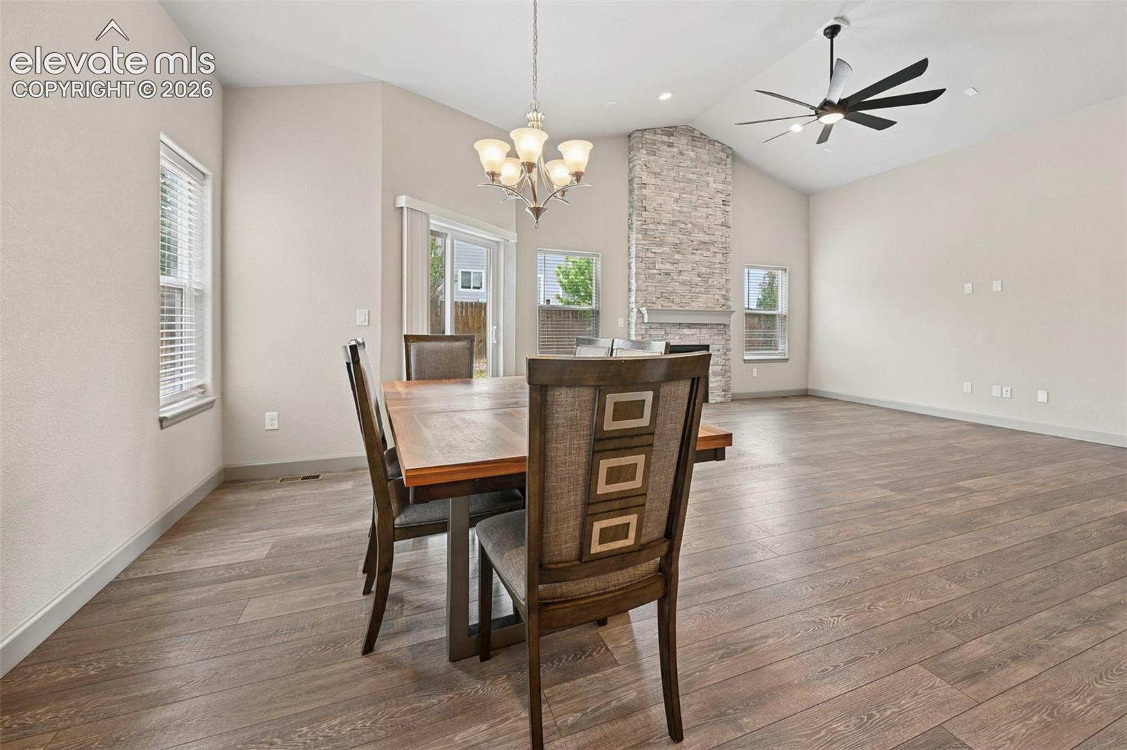 Vaulted ceiling featuring a stacked stone fireplace, wood-finish flooring, a multi-blade ceiling fan, and a chandelier