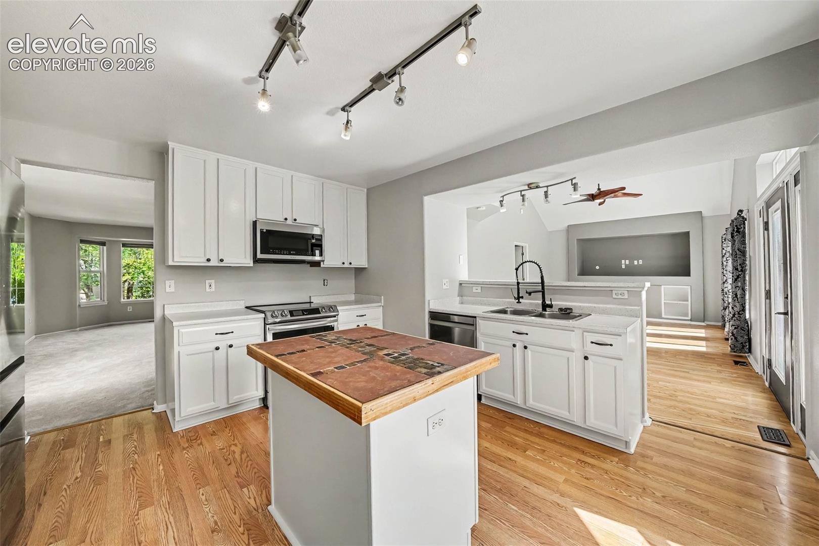 Kitchen featuring white cabinetry, stainless steel appliances, a center island with a tiled countertop, and hardwood flooring
