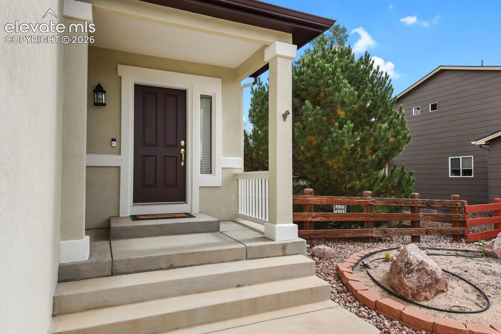 Stucco exterior with a covered porch featuring square columns, a dark panel door, a side light, and concrete steps
