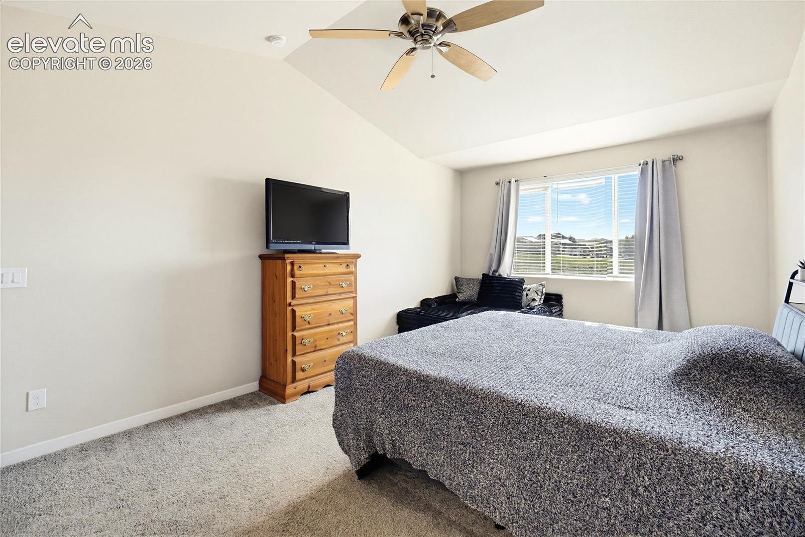 Vaulted ceiling featuring a central multi-blade ceiling fan, wall-to-wall carpeting, and a multi-pane window with horizontal blinds