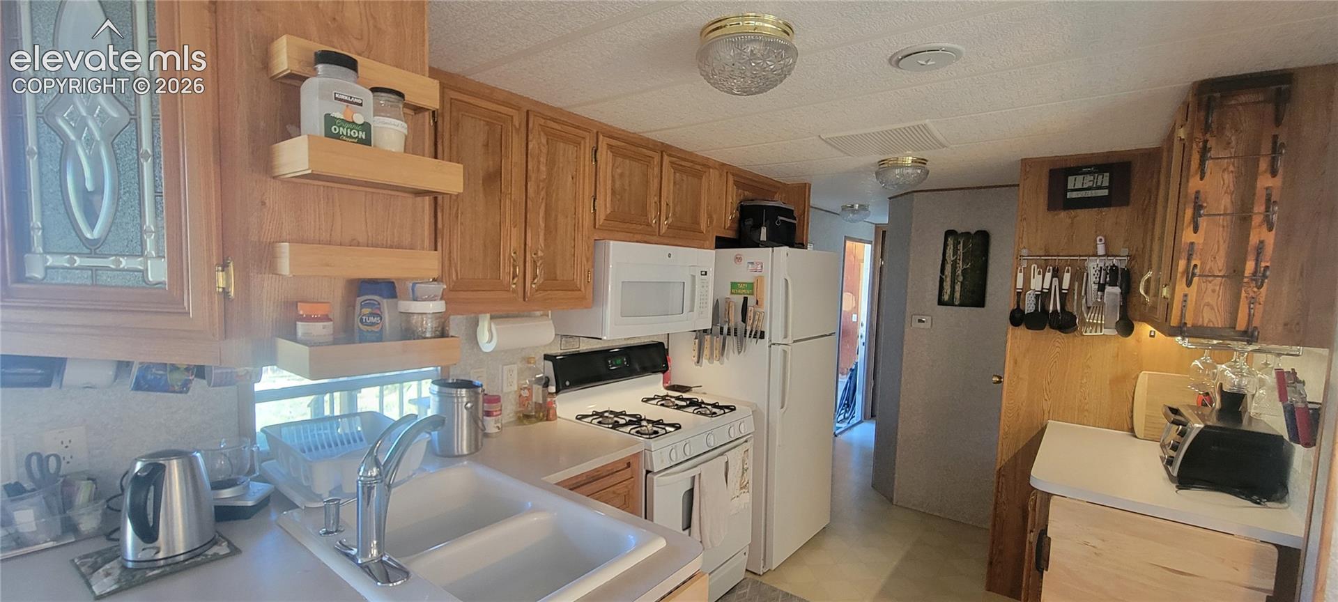 Kitchen featuring oak-finish cabinetry, white appliances, a gas range, and a double basin sink with a chrome faucet