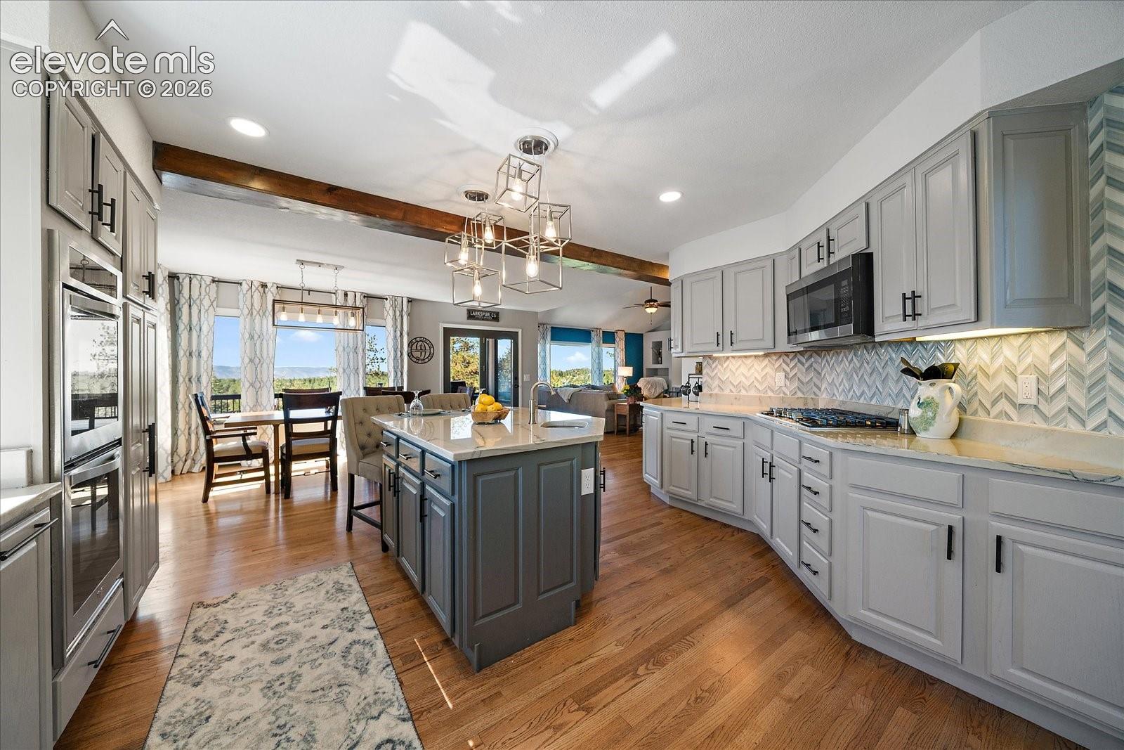 Kitchen featuring grey shaker-style cabinetry, central island with seating, stone countertops, herringbone-patterned backsplash, and wood-finish flooring