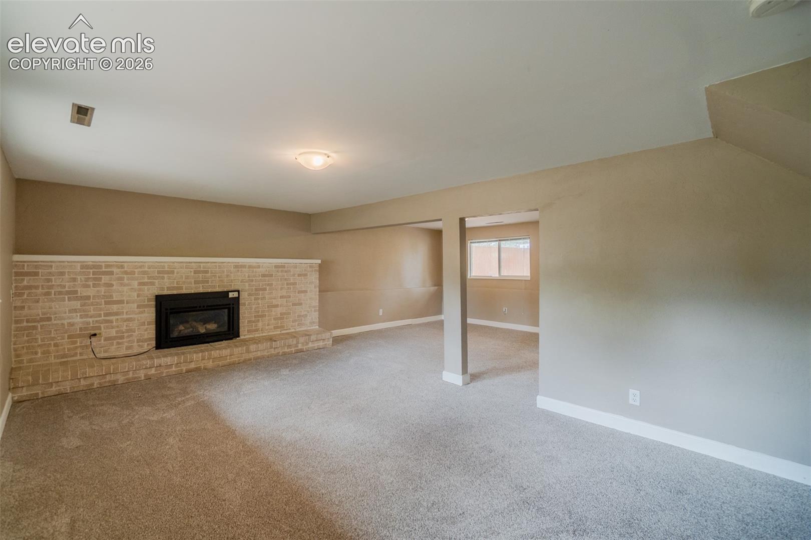 Recessed fireplace with a light brick surround, neutral tone carpeting, and a flush mount ceiling light fixture