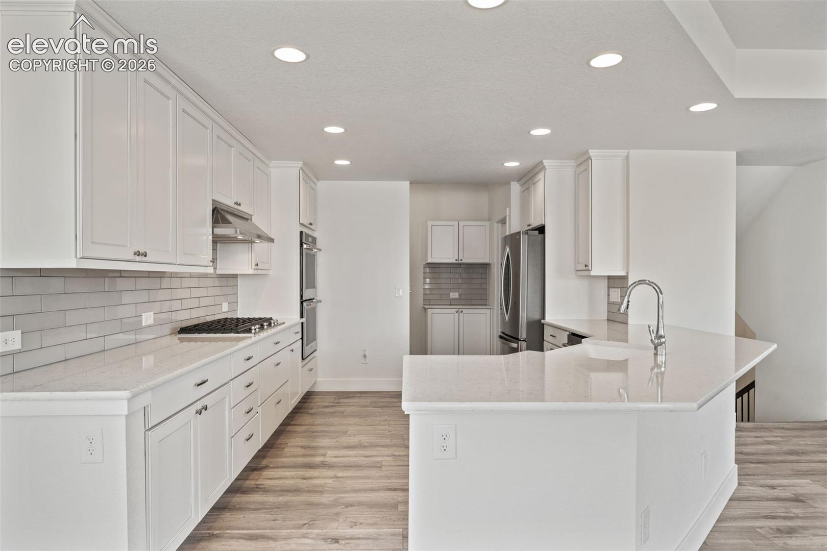 White shaker cabinetry, light-toned countertops, subway tile backsplash, stainless steel appliances, and wood-finish LVP flooring