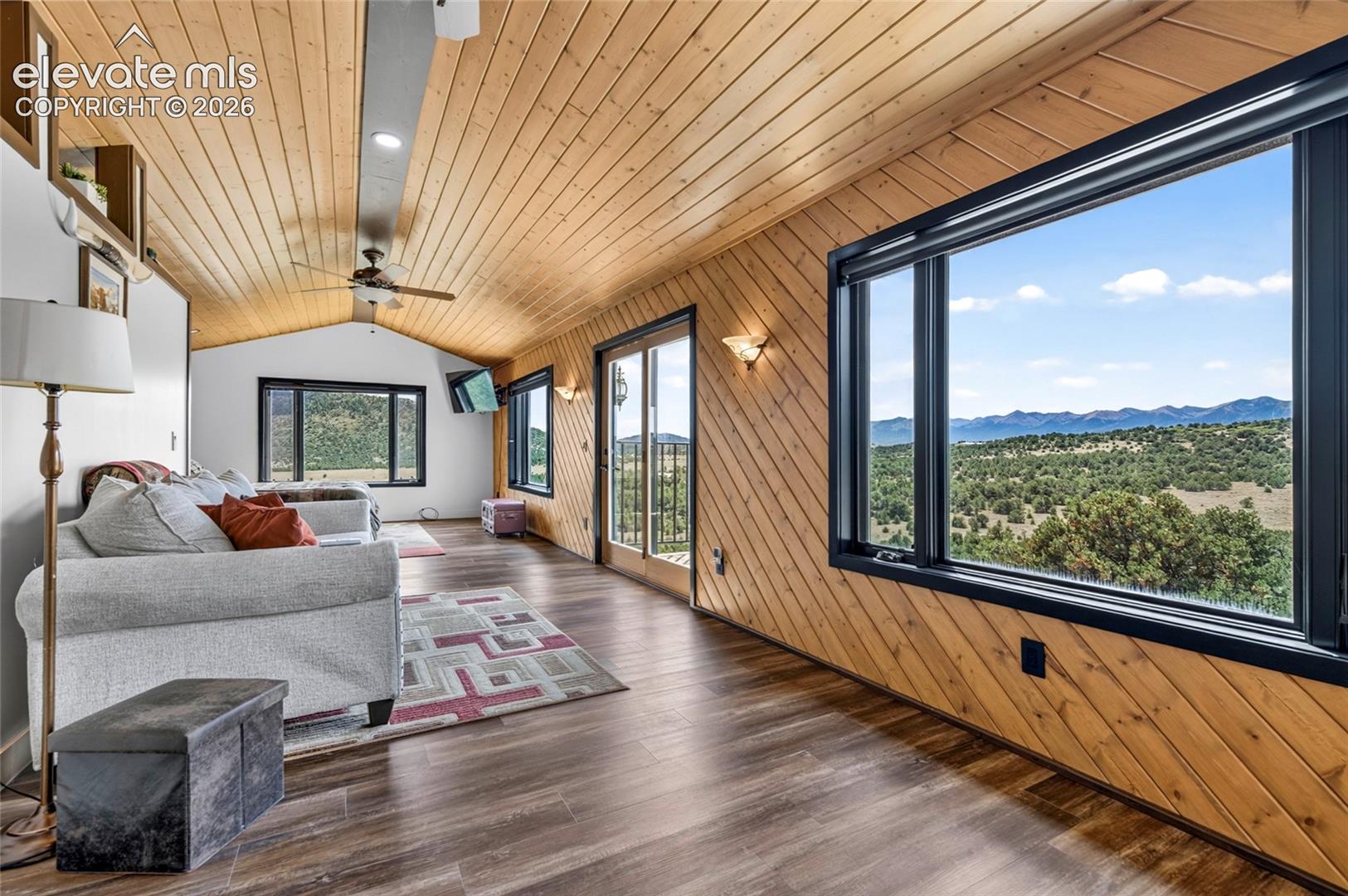 Wood-finish flooring with an angled wood-paneled wall, vaulted wood-plank ceiling, and large fixed-pane window
