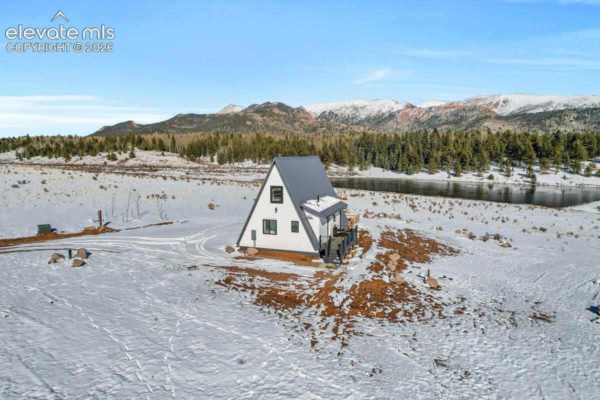 A-frame exterior featuring white siding, a metal roof, and an attached deck, set against a mountain and river landscape