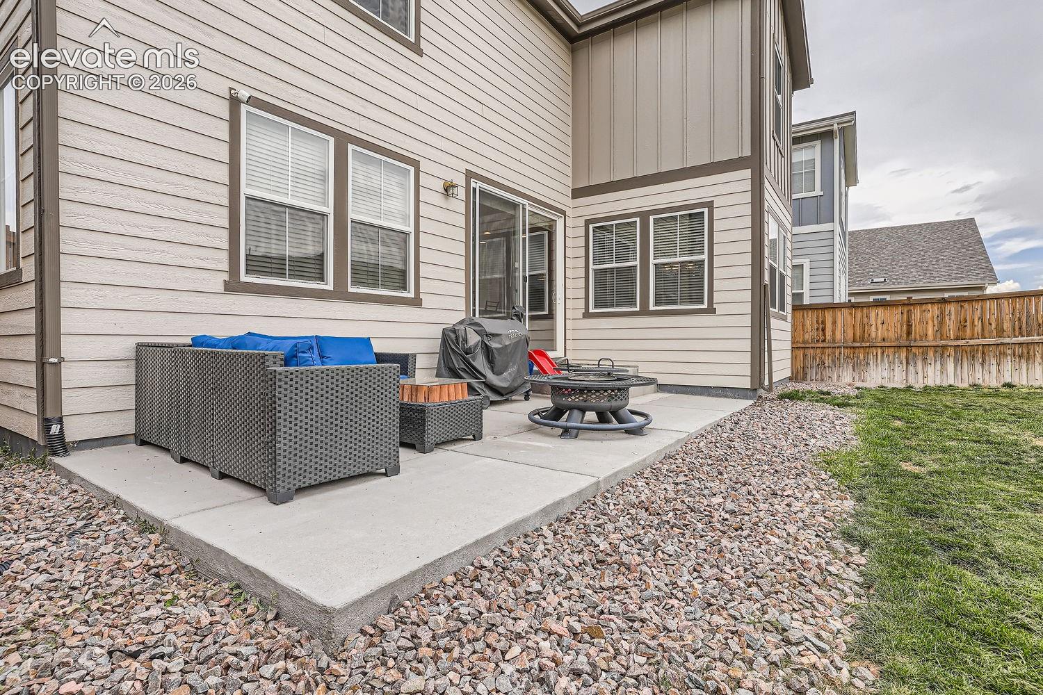 Rear exterior featuring horizontal lap siding, vertical board-and-batten accents, a concrete patio, sliding glass door access, and a wood privacy fence