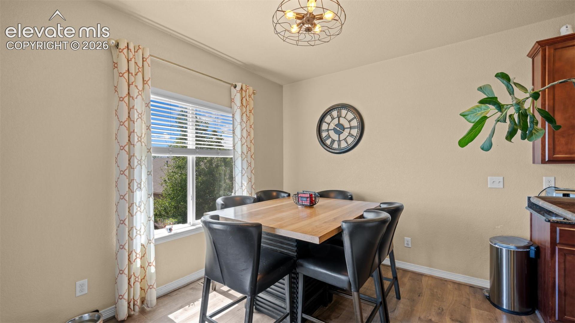 Open-concept dining area featuring a window with integrated blinds, wood-finish flooring, and a decorative ceiling light fixture