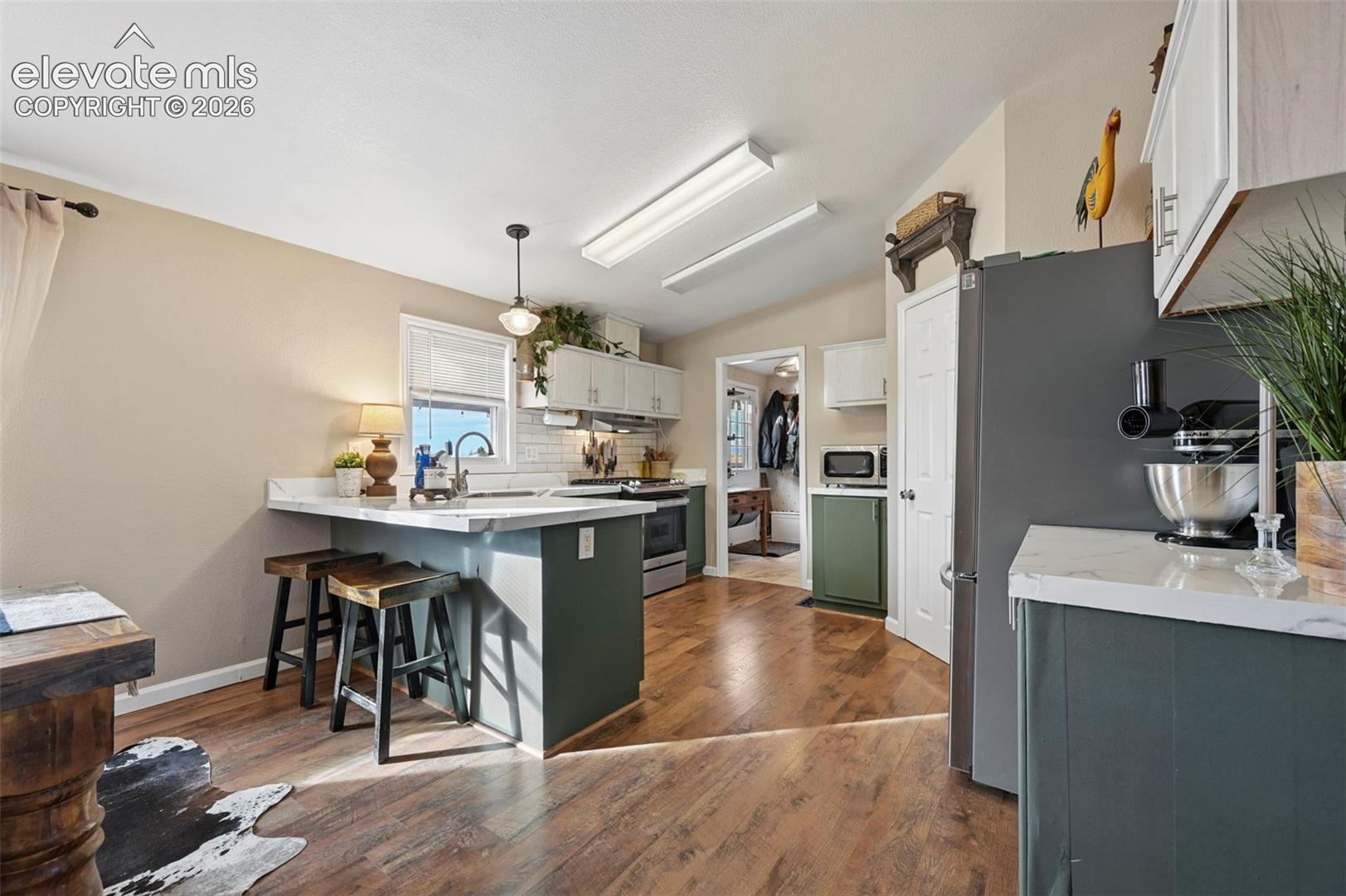Kitchen featuring a peninsula with solid-surface countertops, two-tone cabinetry, white subway tile backsplash, and wood-finish flooring
