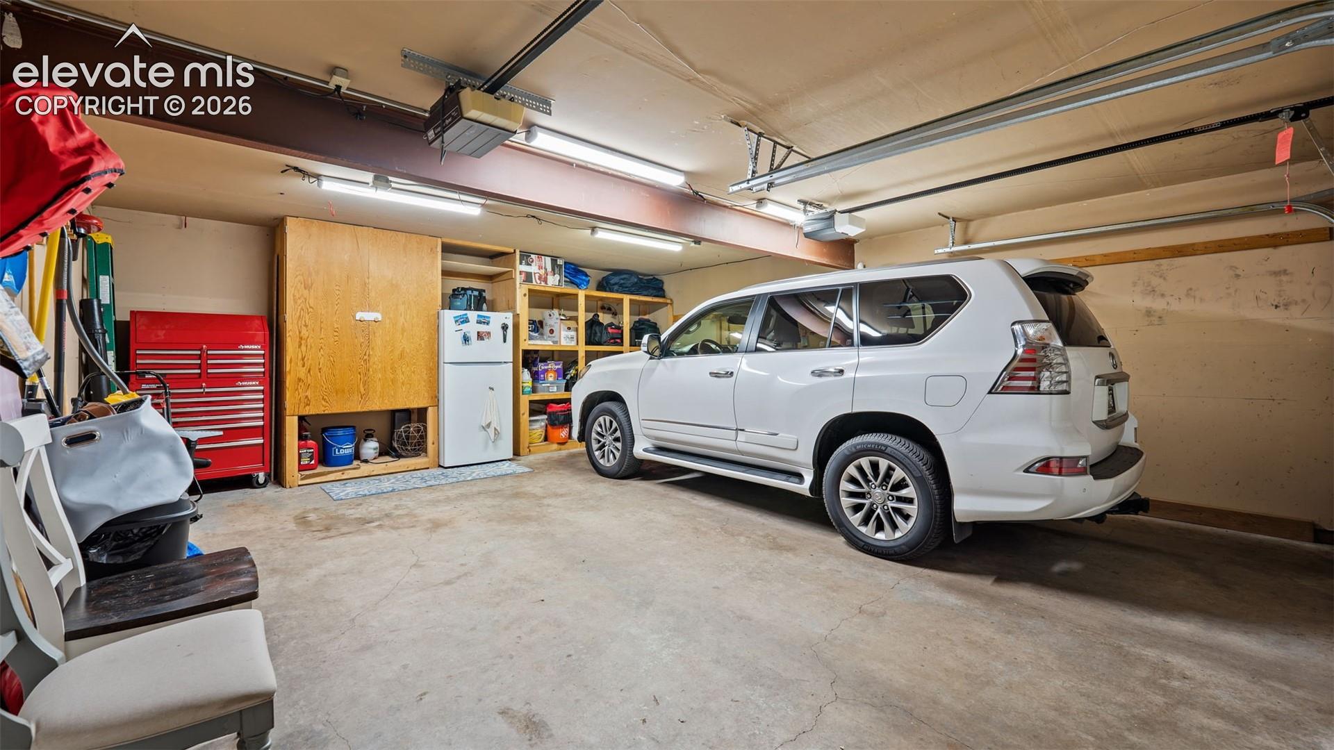 Two-car garage featuring built-in wood shelving, dual garage door openers, and fluorescent overhead lighting