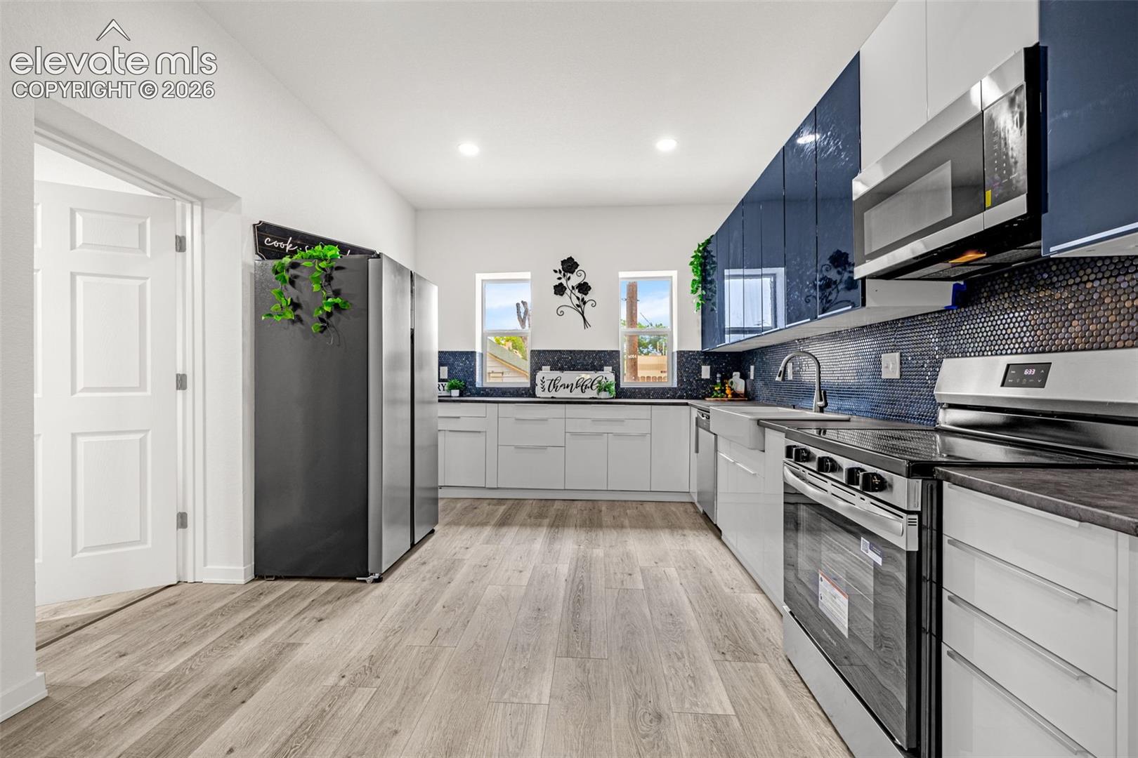 Contemporary kitchen featuring wood-finish flooring, white cabinetry, and dark blue mosaic tile backsplash