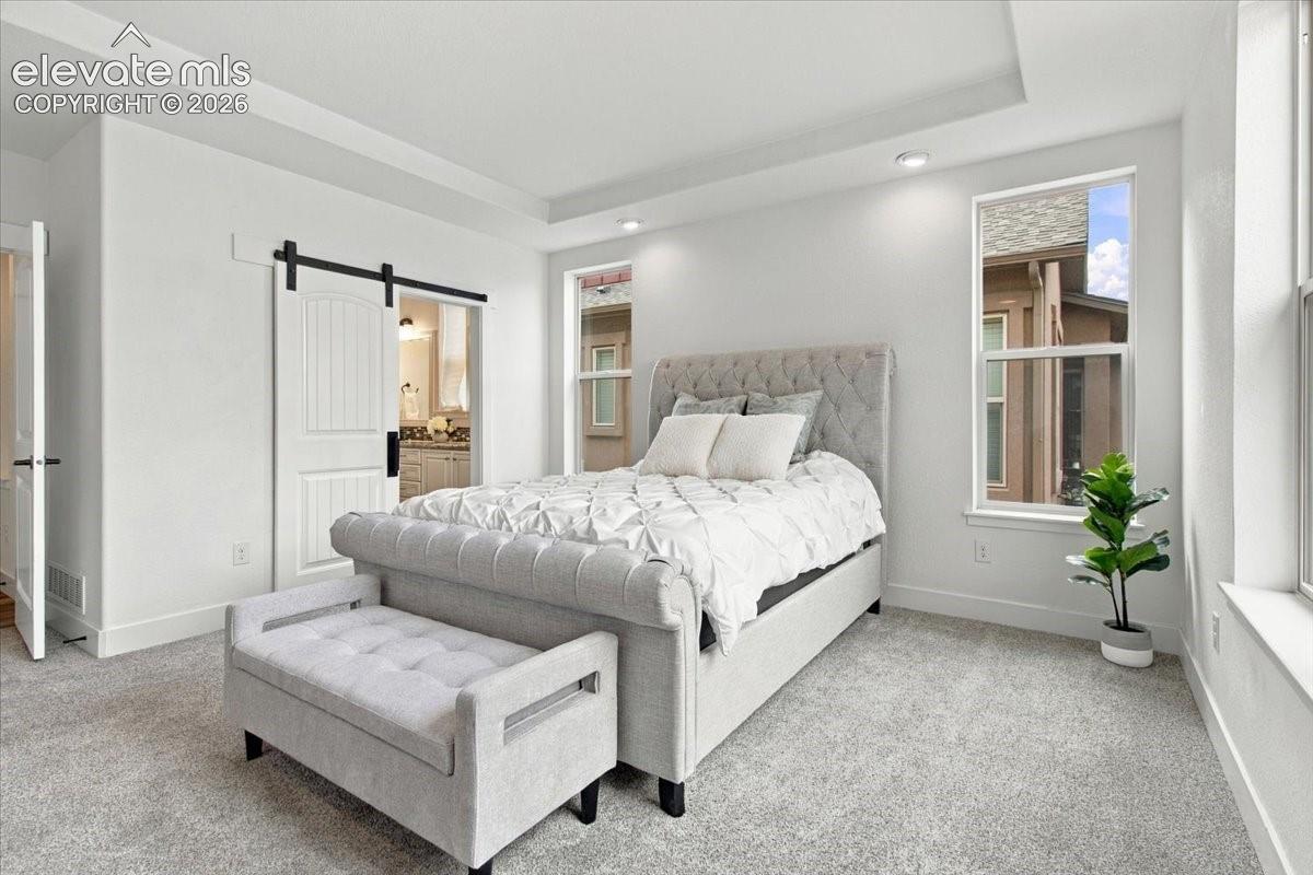 Tray ceiling, recessed lighting, neutral carpeting, and white sliding barn door